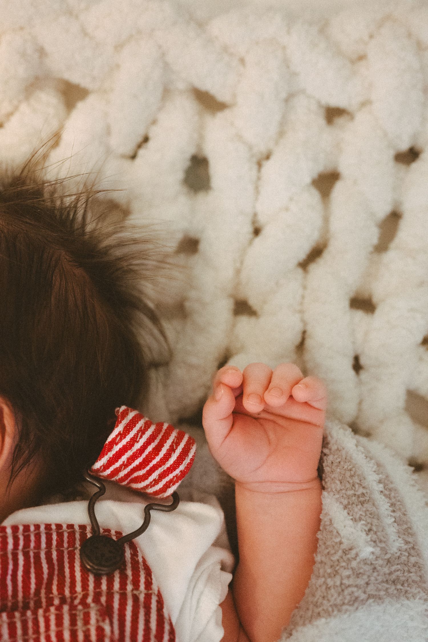 Close-up details of sleeping baby on white chunky knit blanket wearing red and white stripes.