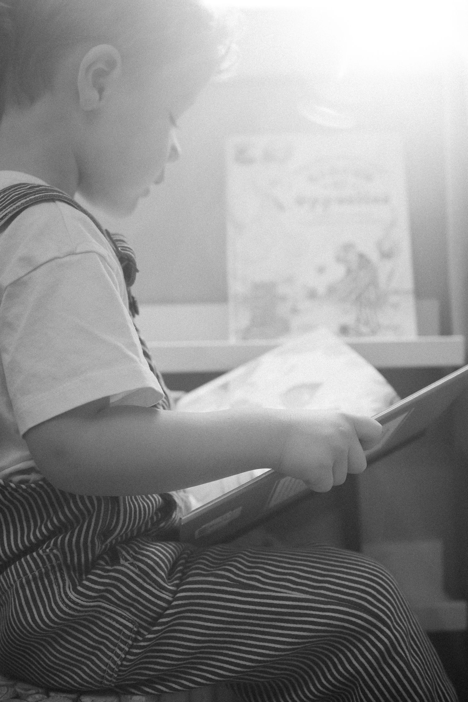 A black and white photo shows a child reading a book in striped clothing.