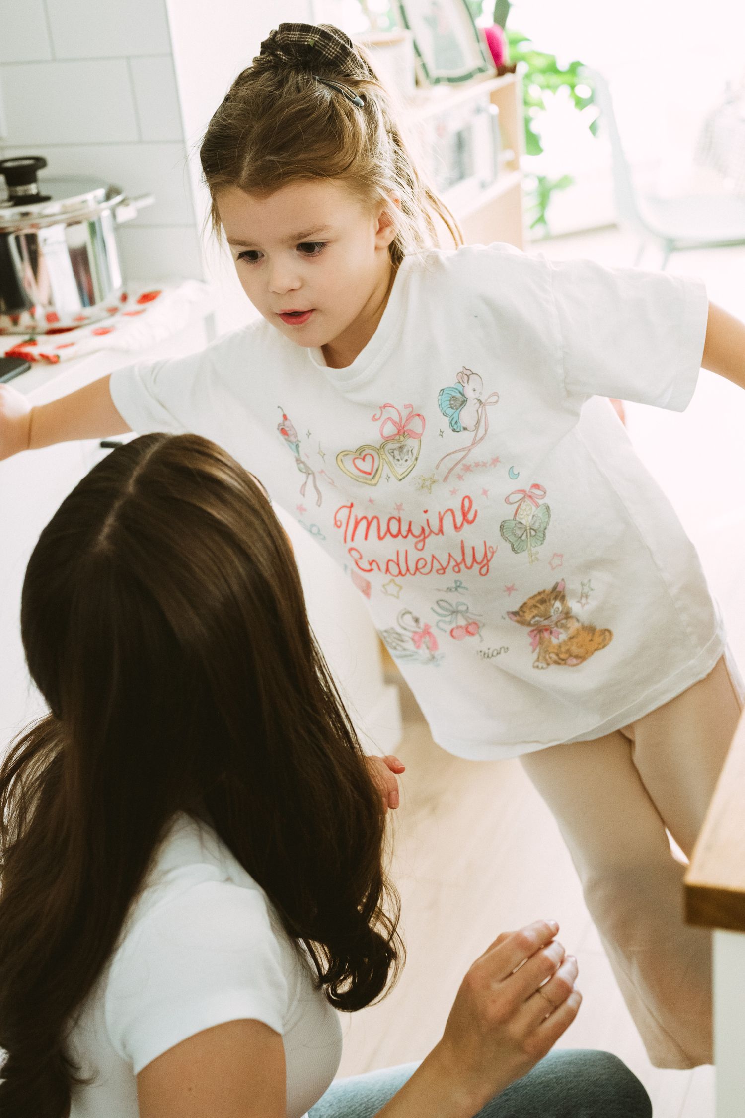 Children wearing white t-shirts with colorful designs gather together in a bright indoor space.