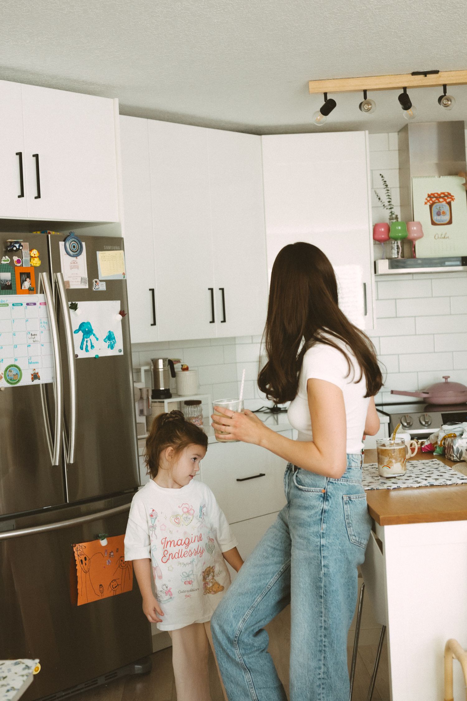 A casual kitchen scene with people in denim and white shirts standing near stainless steel appliances.