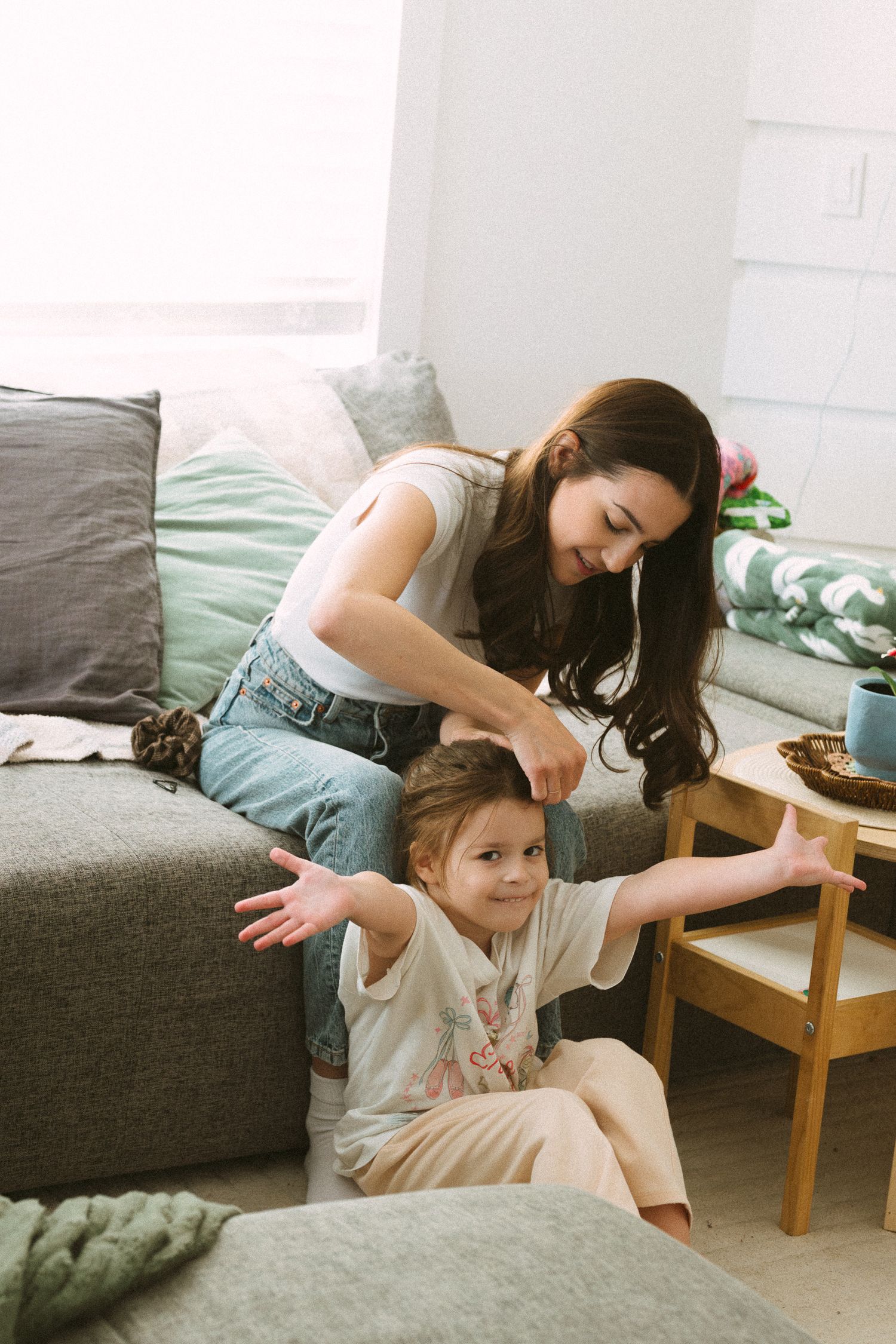 A parent and child share a playful moment together on a gray couch in a bright, modern living room.