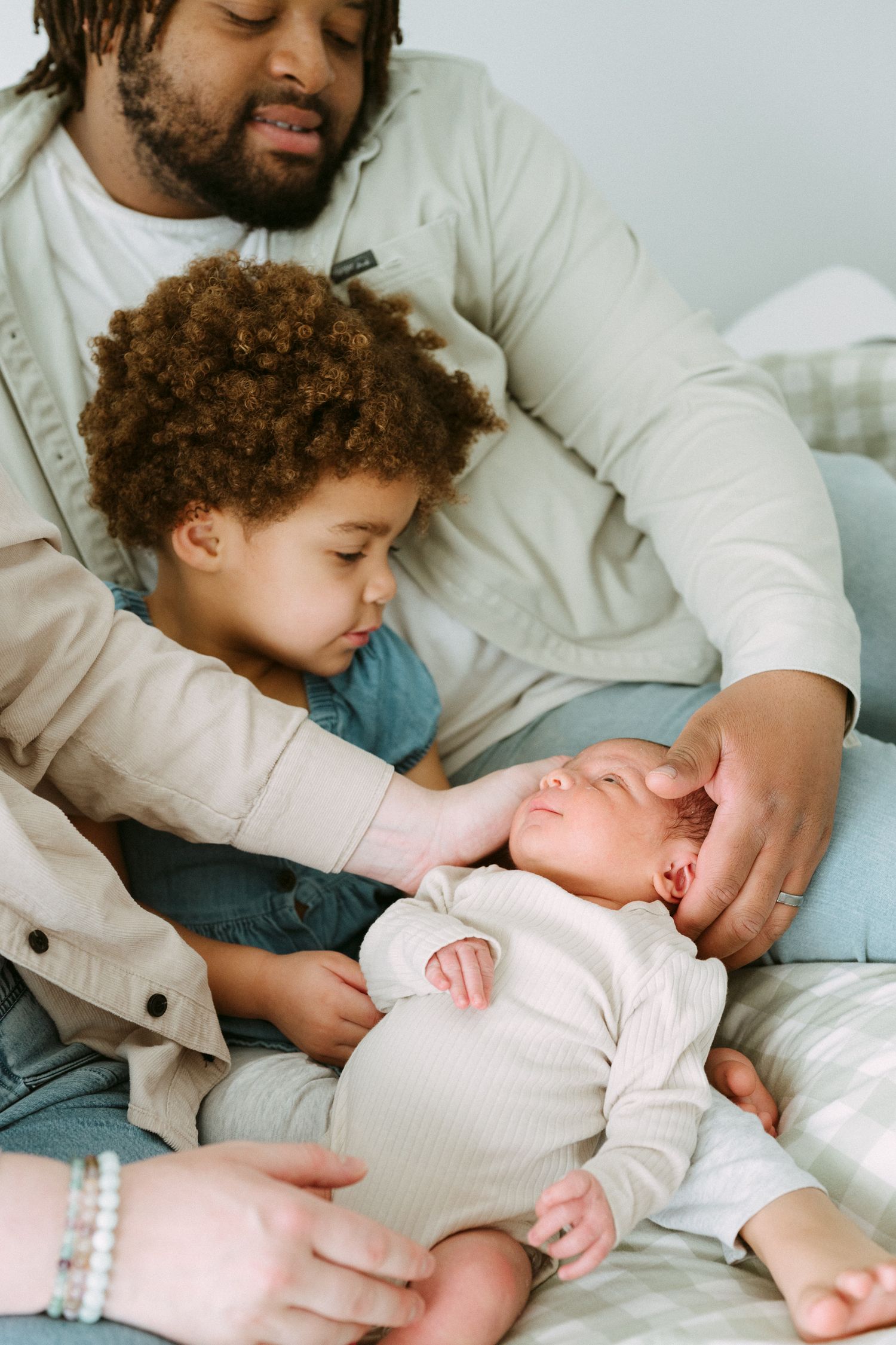 Father and toddler gently bonding with newborn baby on bed.
