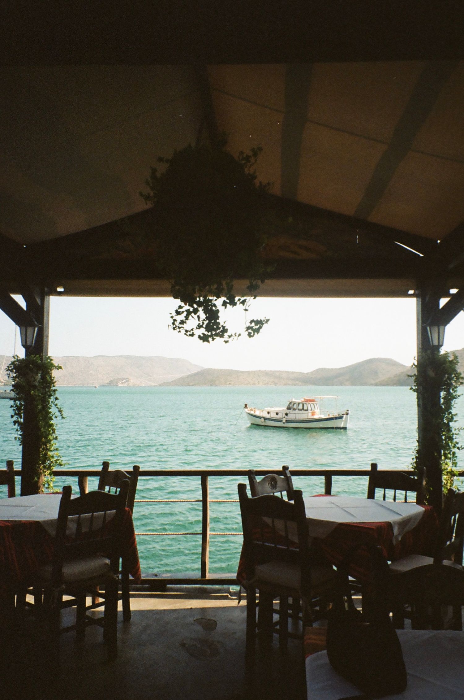Seaside restaurant terrace framing a view of a small fishing boat on crystal blue waters.