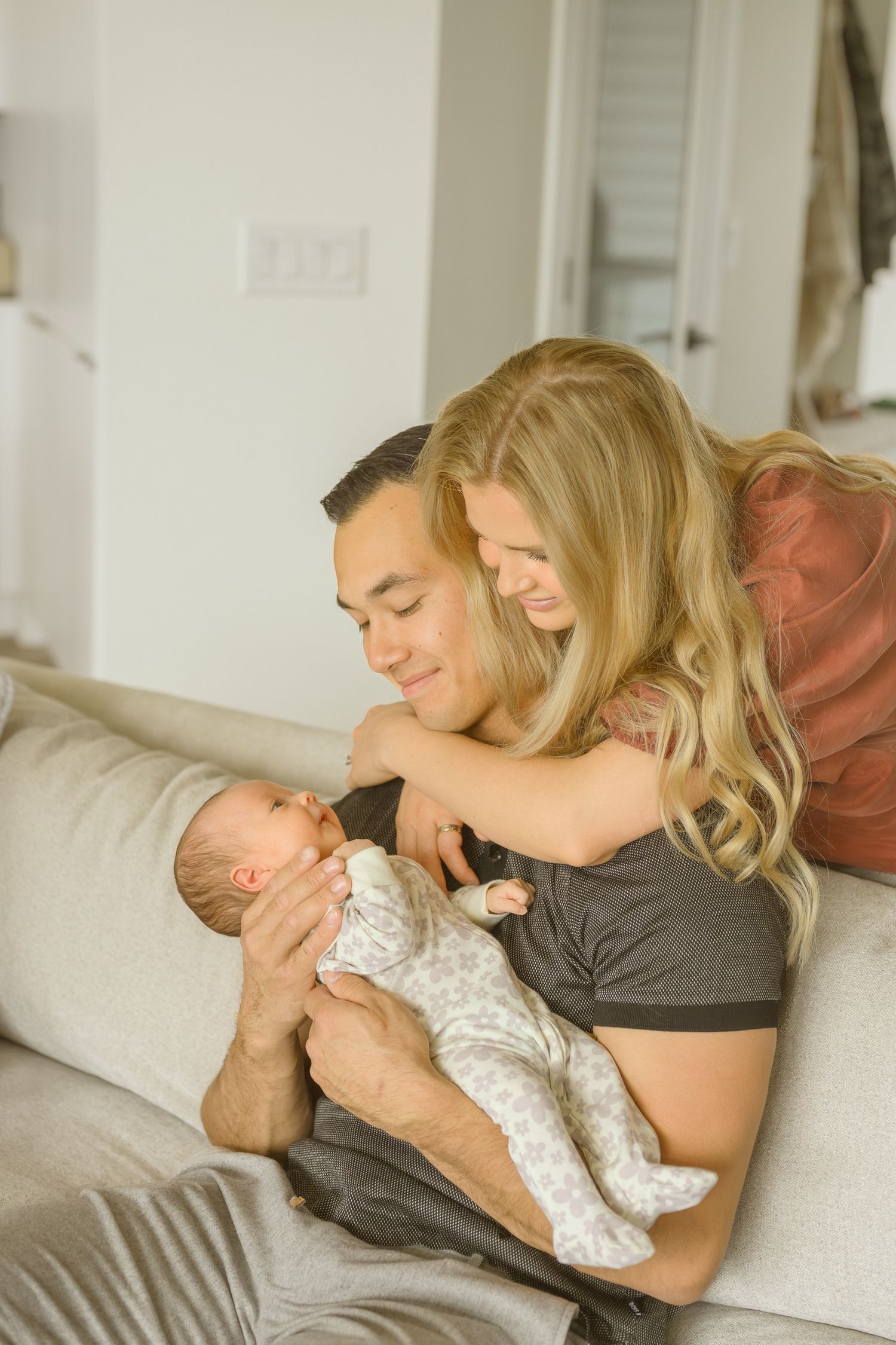 Parents on white couch lovingly holding and looking at their newborn baby.
