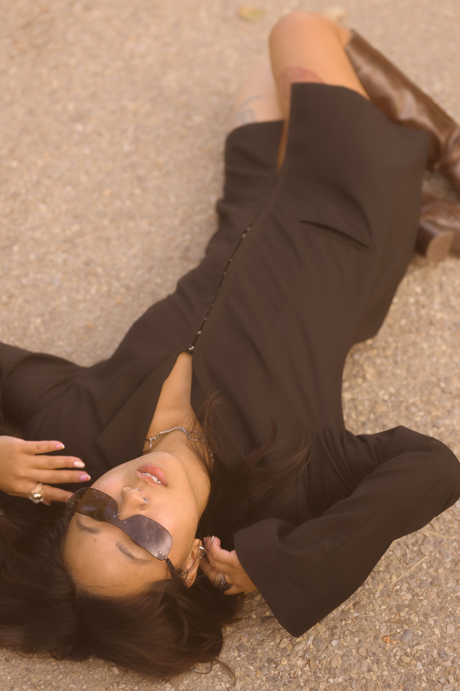 Artistic fashion photo of model lying on concrete in black blazer dress.