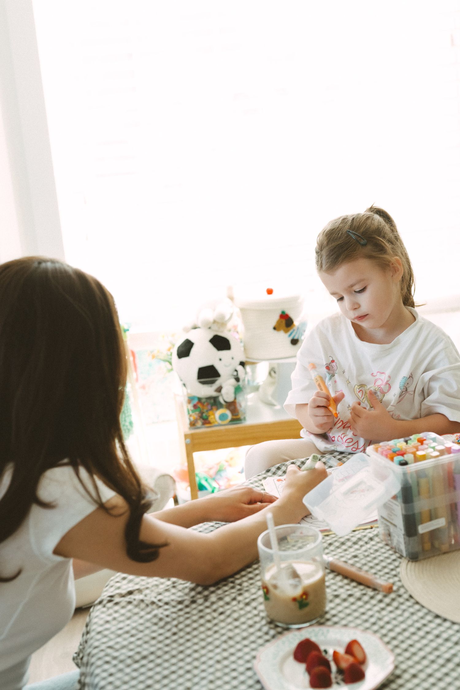 Two children enjoying snacks and drinks at a table with a checkered tablecloth and soccer ball decor in the background.