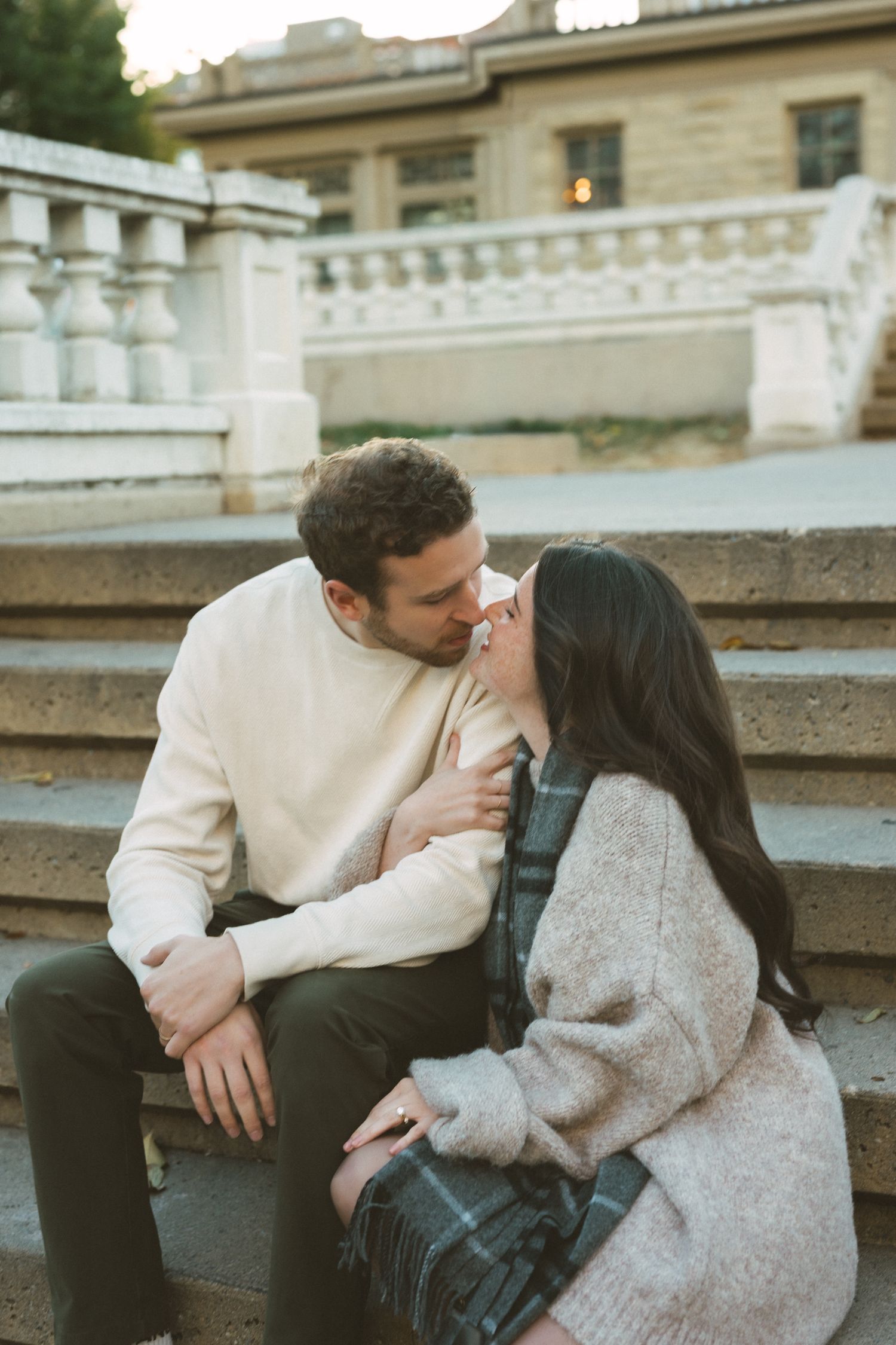 A couple shares an intimate moment while sitting on stone steps wearing casual winter attire.