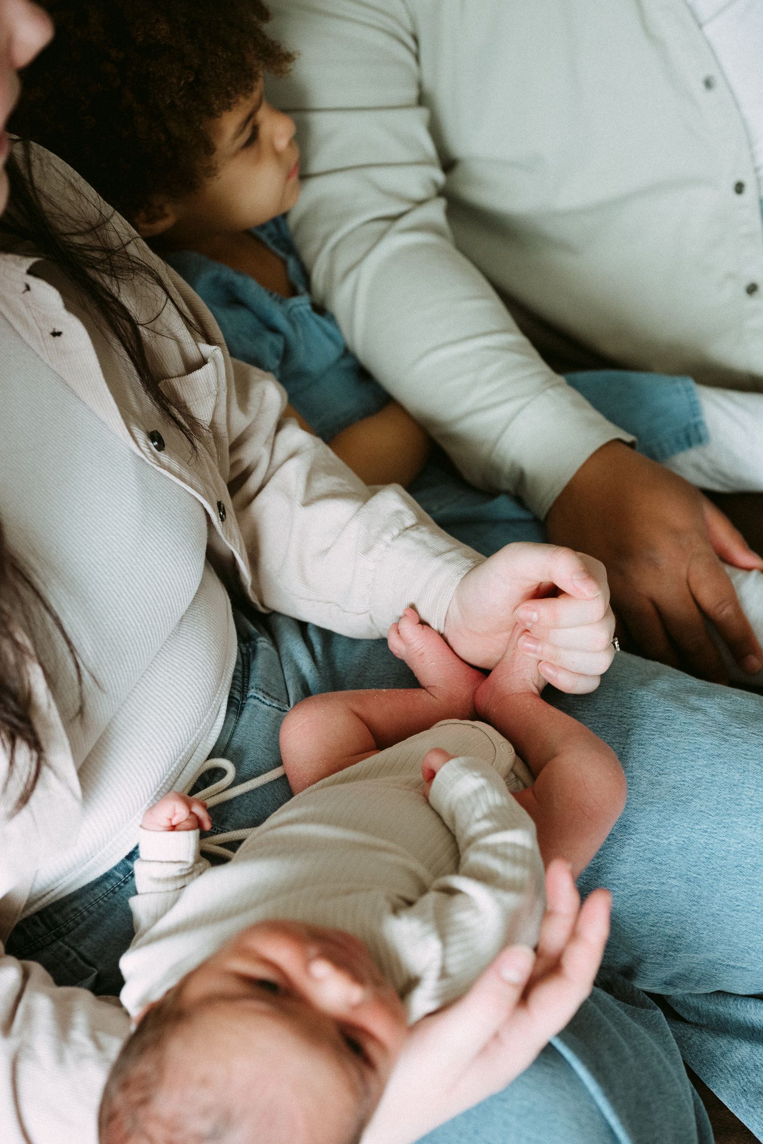 A newborn baby held by family members, with a toddler and parents sitting closely together in a warm, intimate moment.