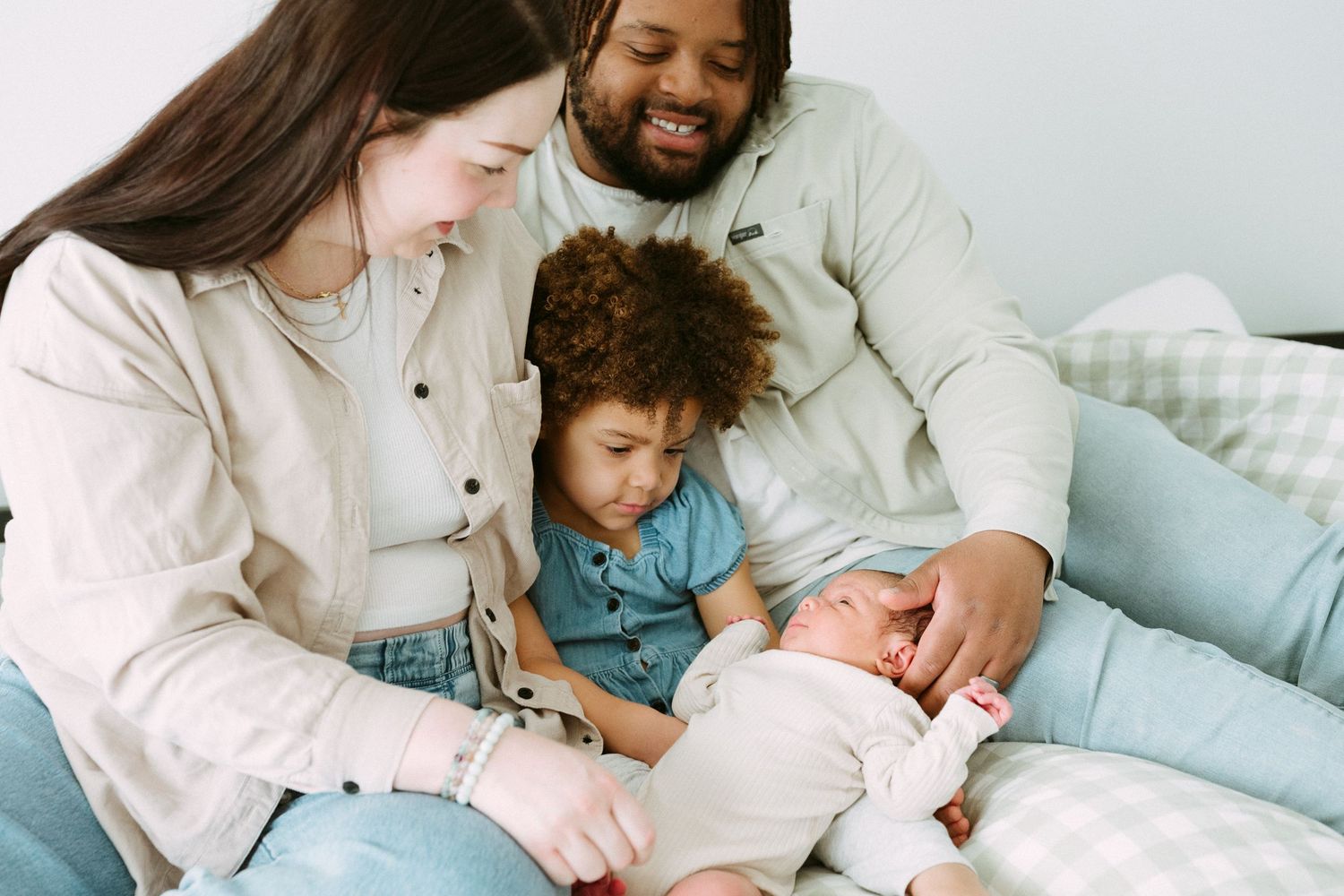 Happy interracial family with toddler and newborn baby bonding together on a couch.