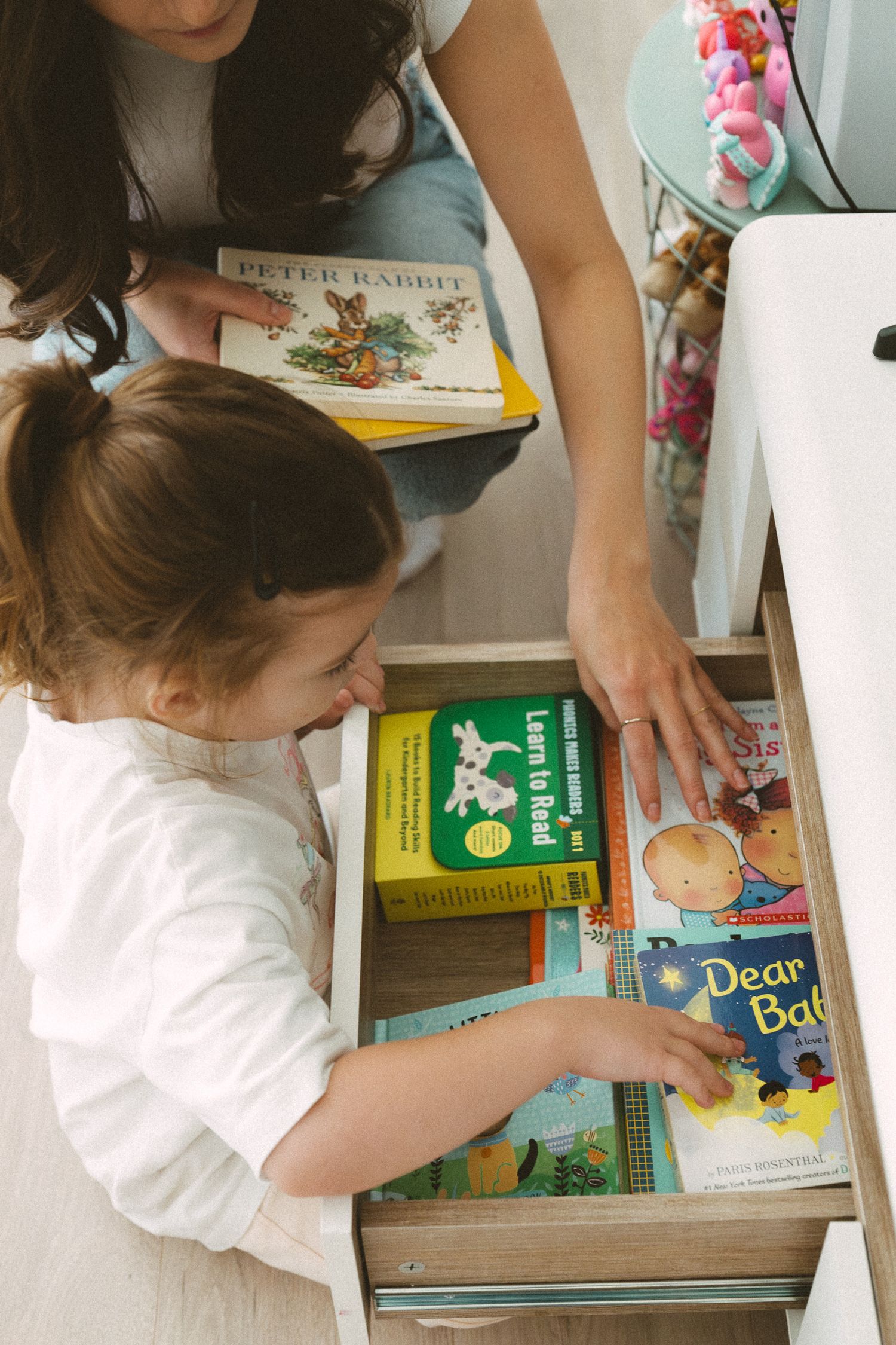 Child exploring a collection of children's books including Peter Rabbit while an adult assists.