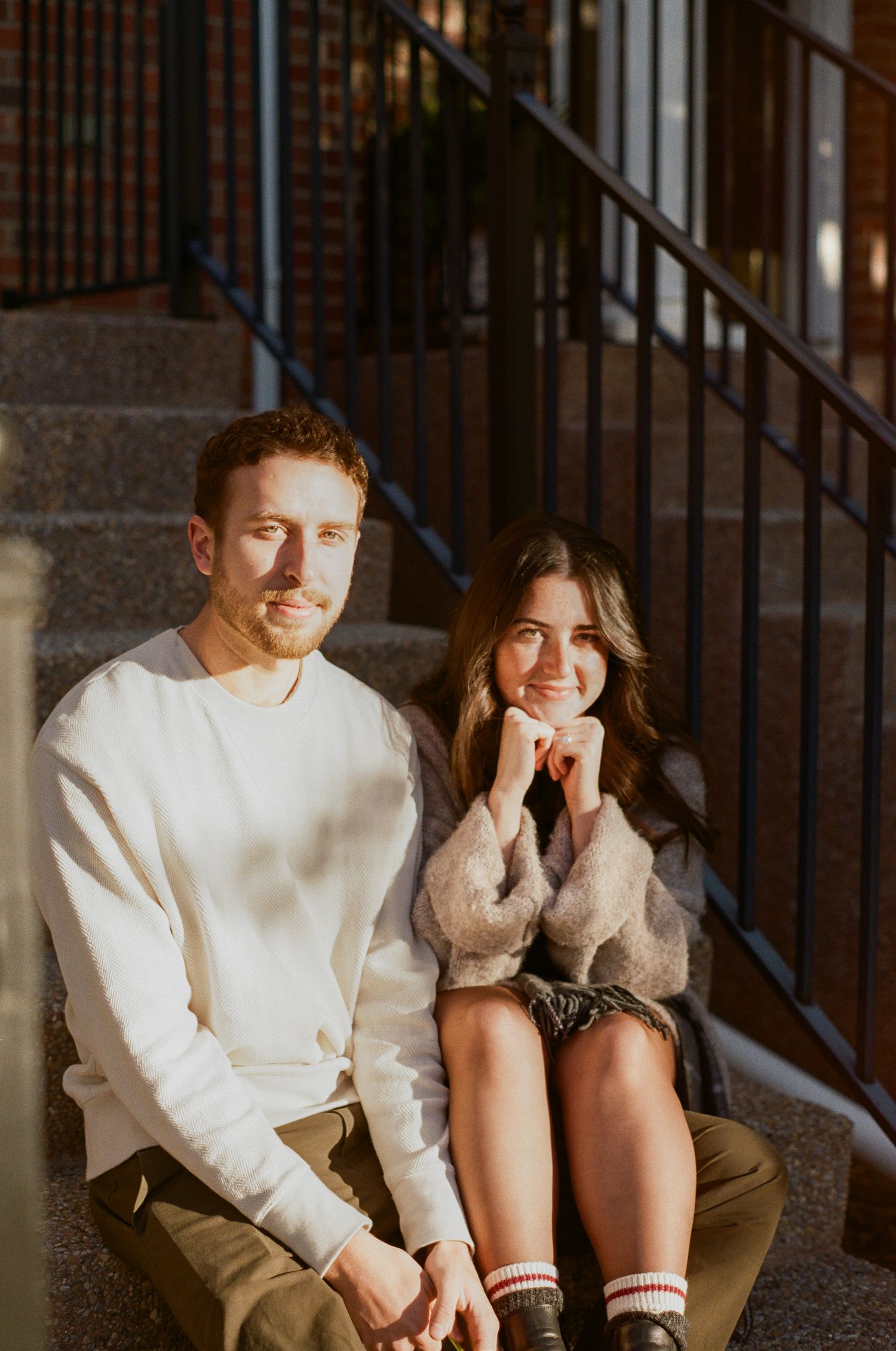 Two people share a cozy moment sitting together on outdoor steps wearing casual autumn attire.