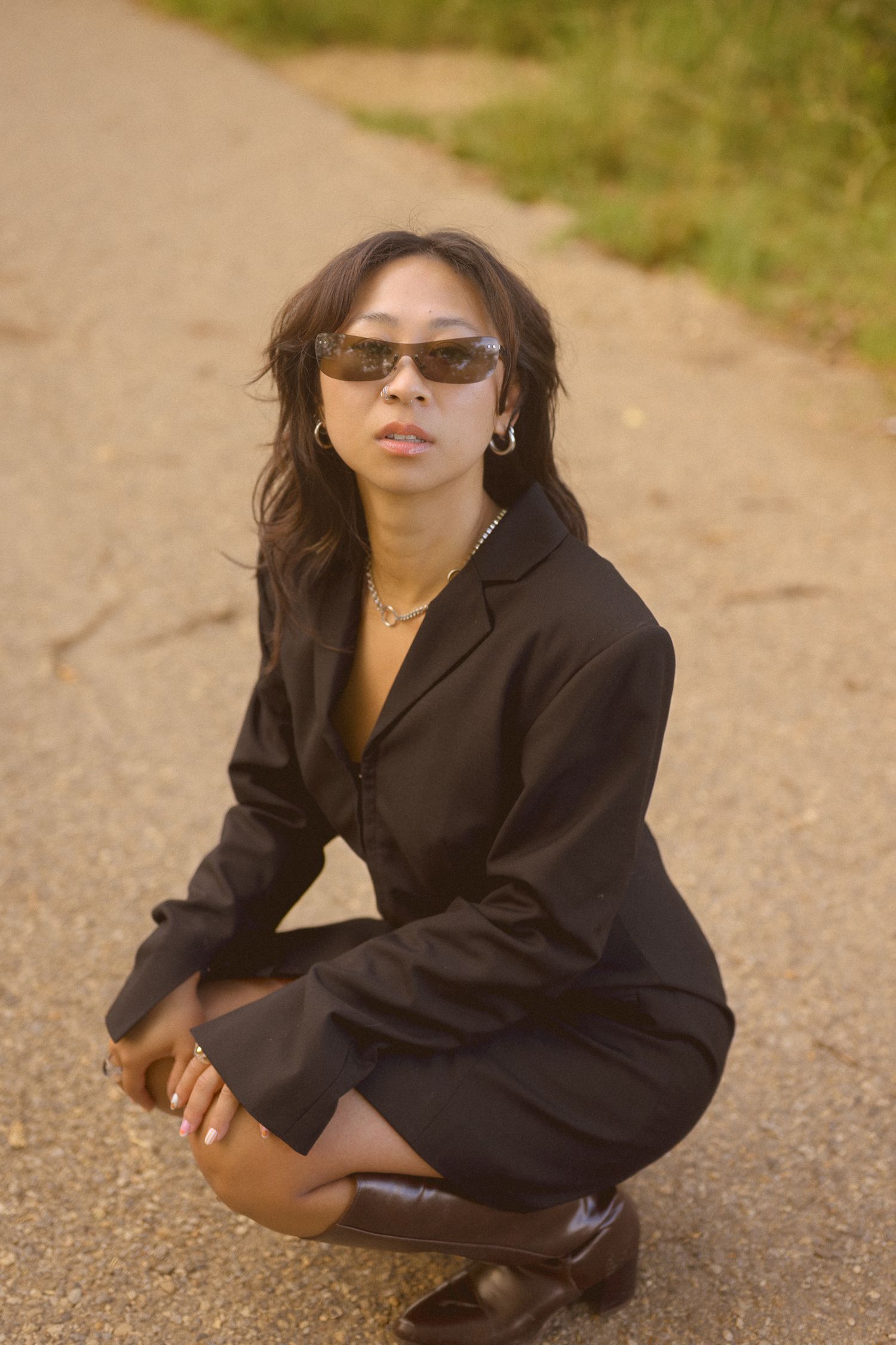 A modern street style look with black blazer dress and retro sunglasses on a dirt path.