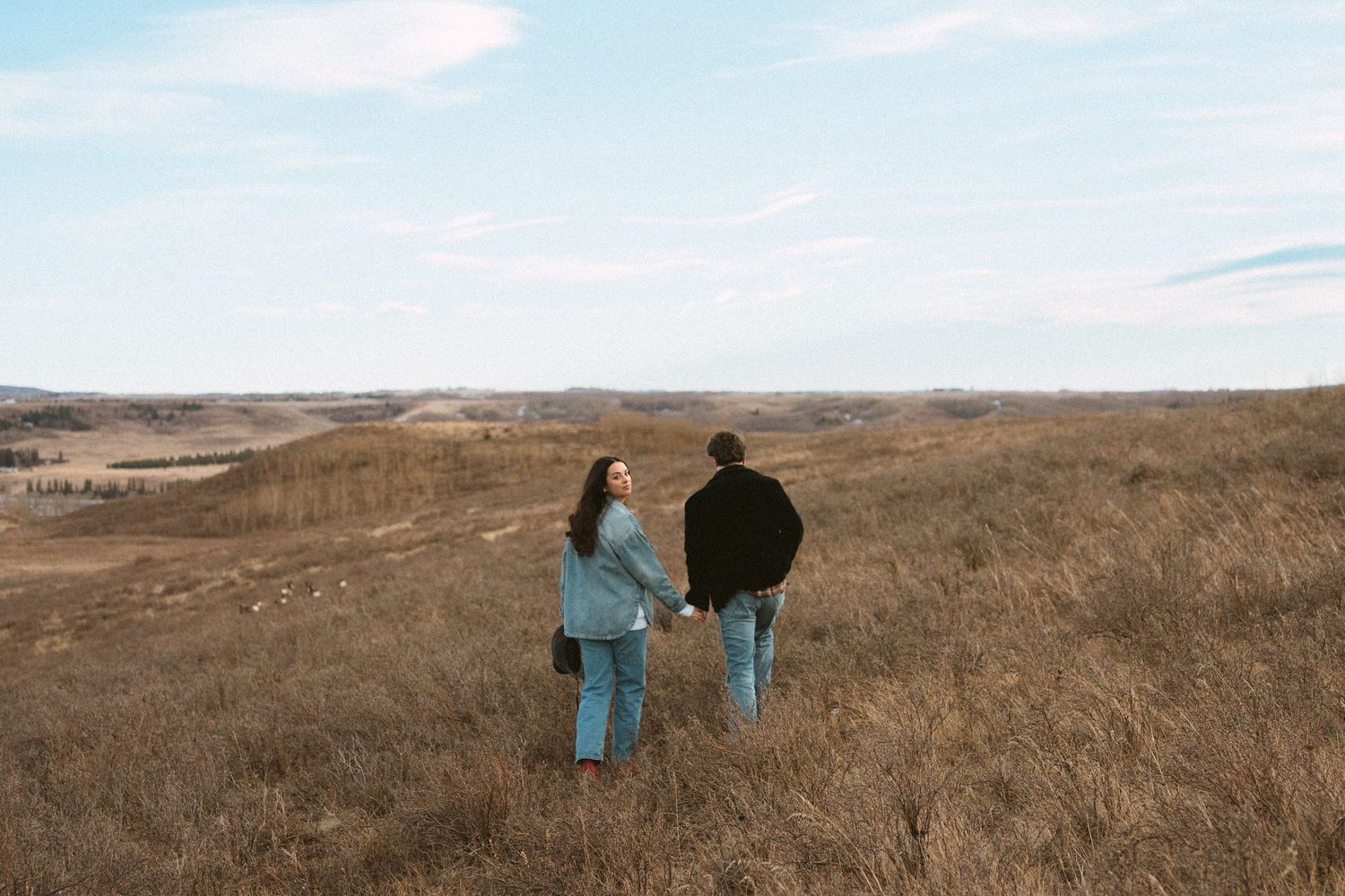 Two people in casual attire walk together through a vast brown field beneath a bright blue sky.