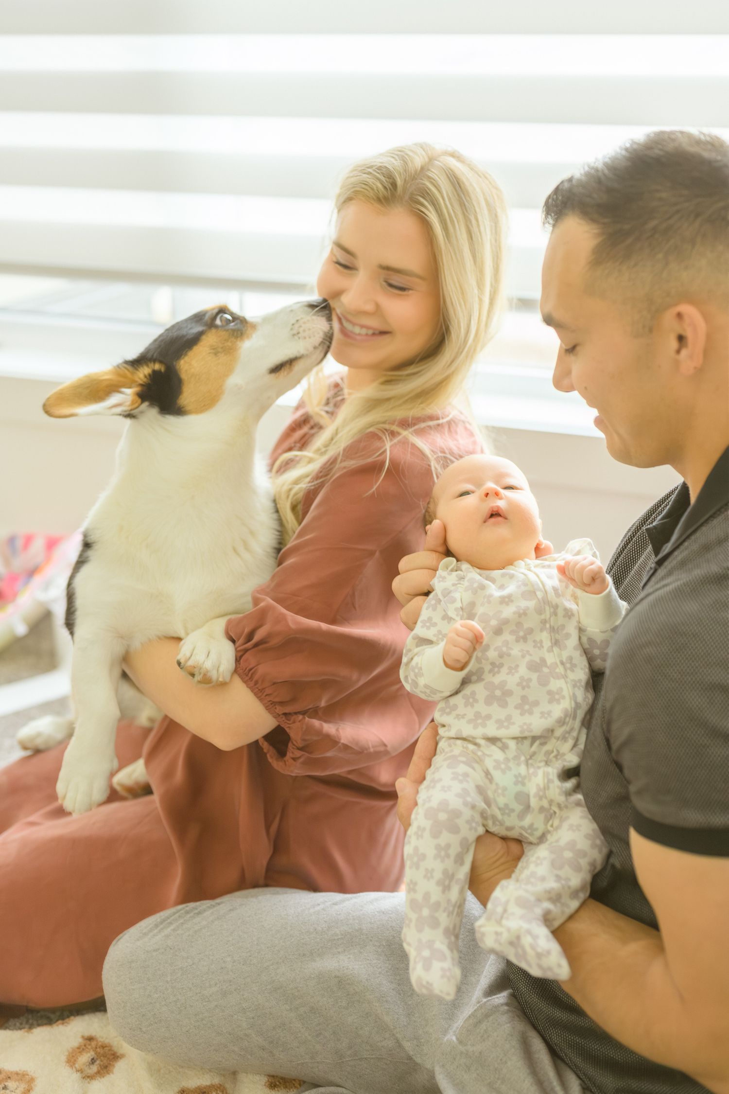 A happy family moment with a playful dog giving kisses while holding their baby.