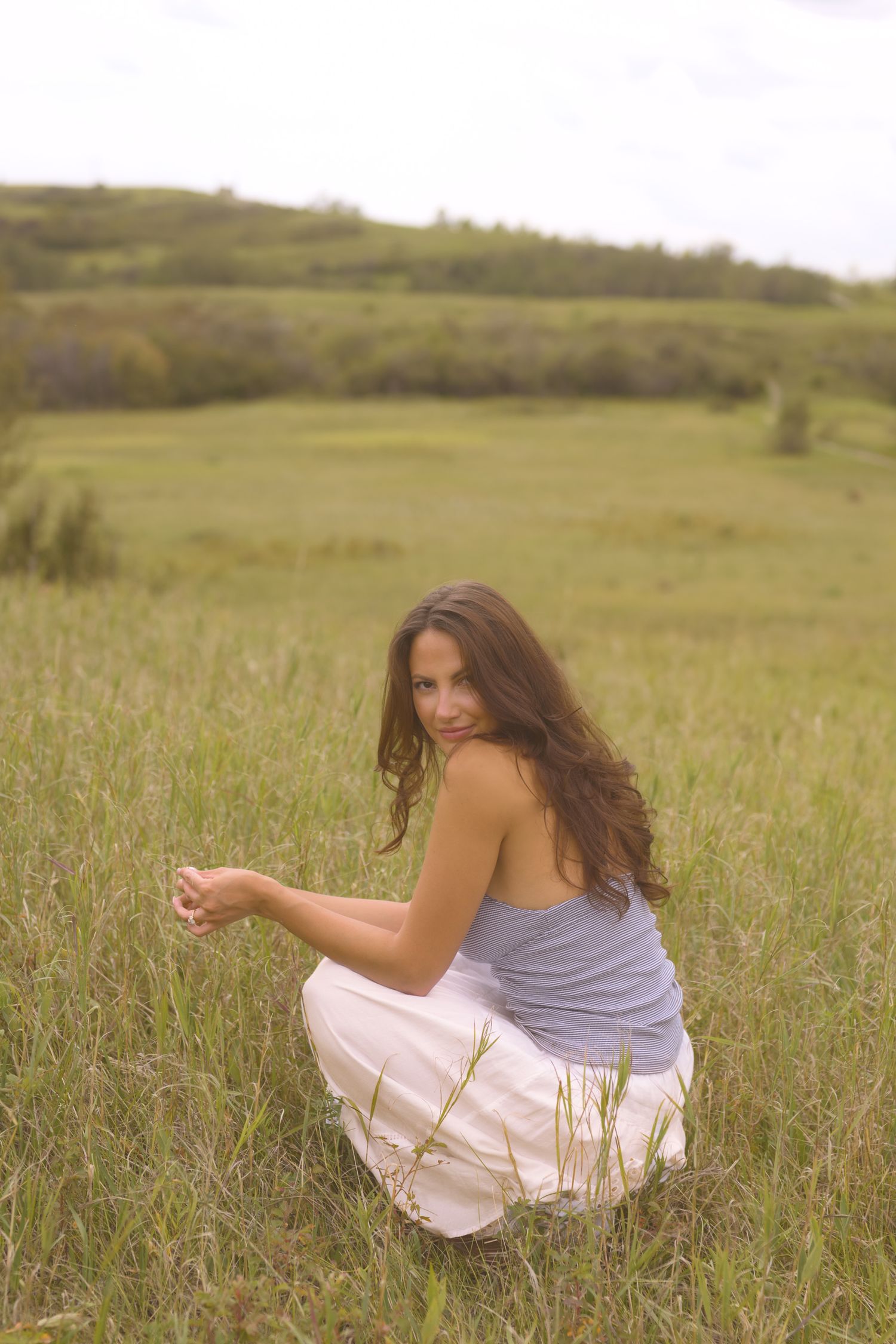 Someone in a white dress sits gracefully in a sunlit meadow of tall grass.