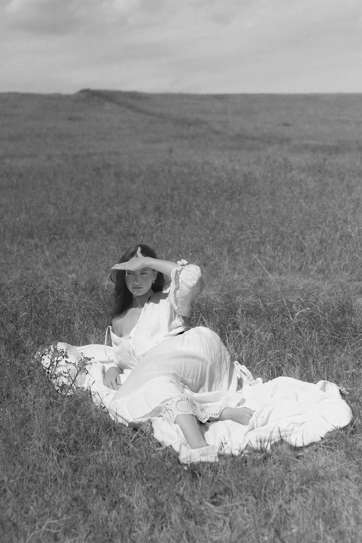 Black and white image of someone lounging in a white dress in a sunlit meadow.