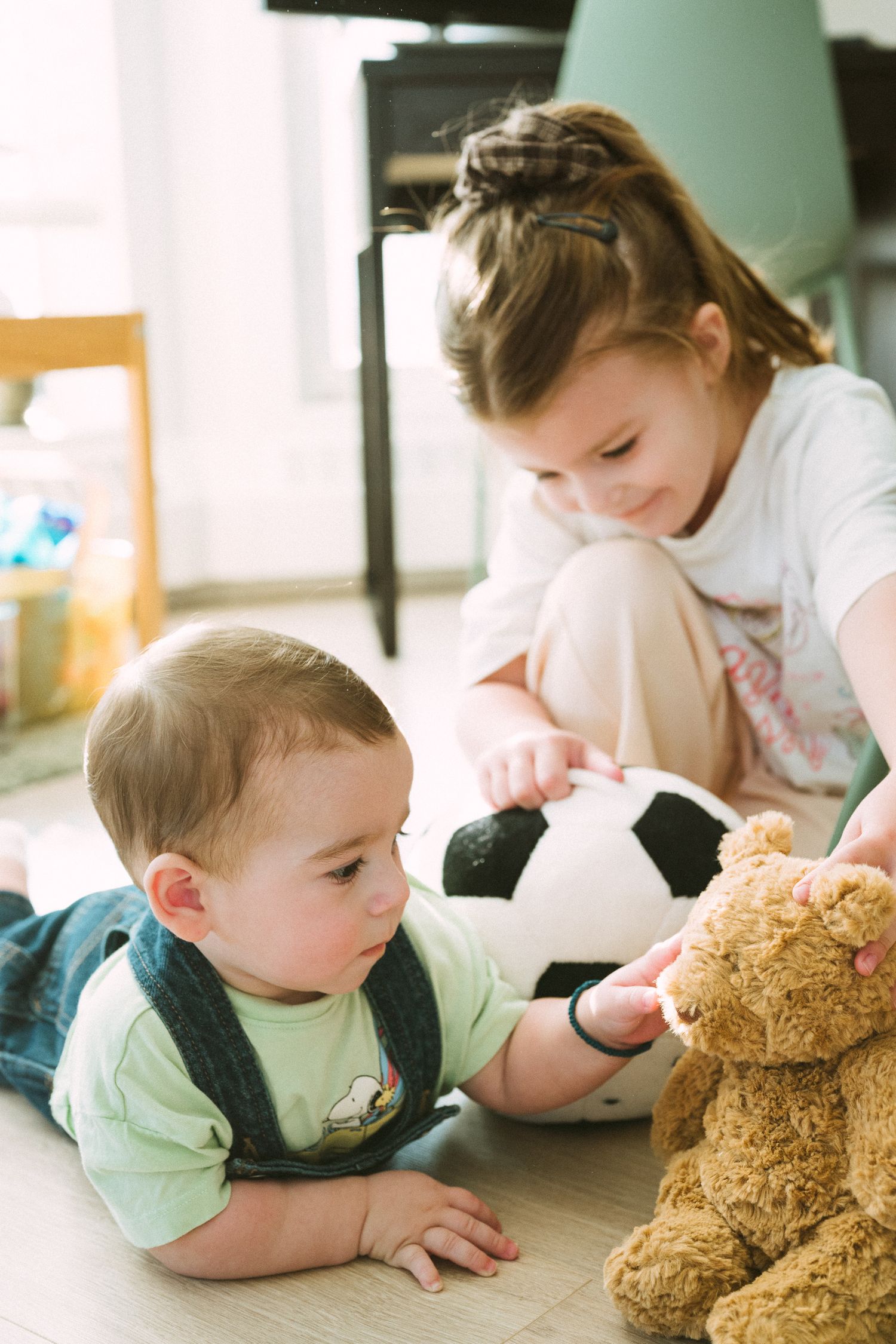 A child playing with a teddy bear while lying on the floor in a sunlit room.