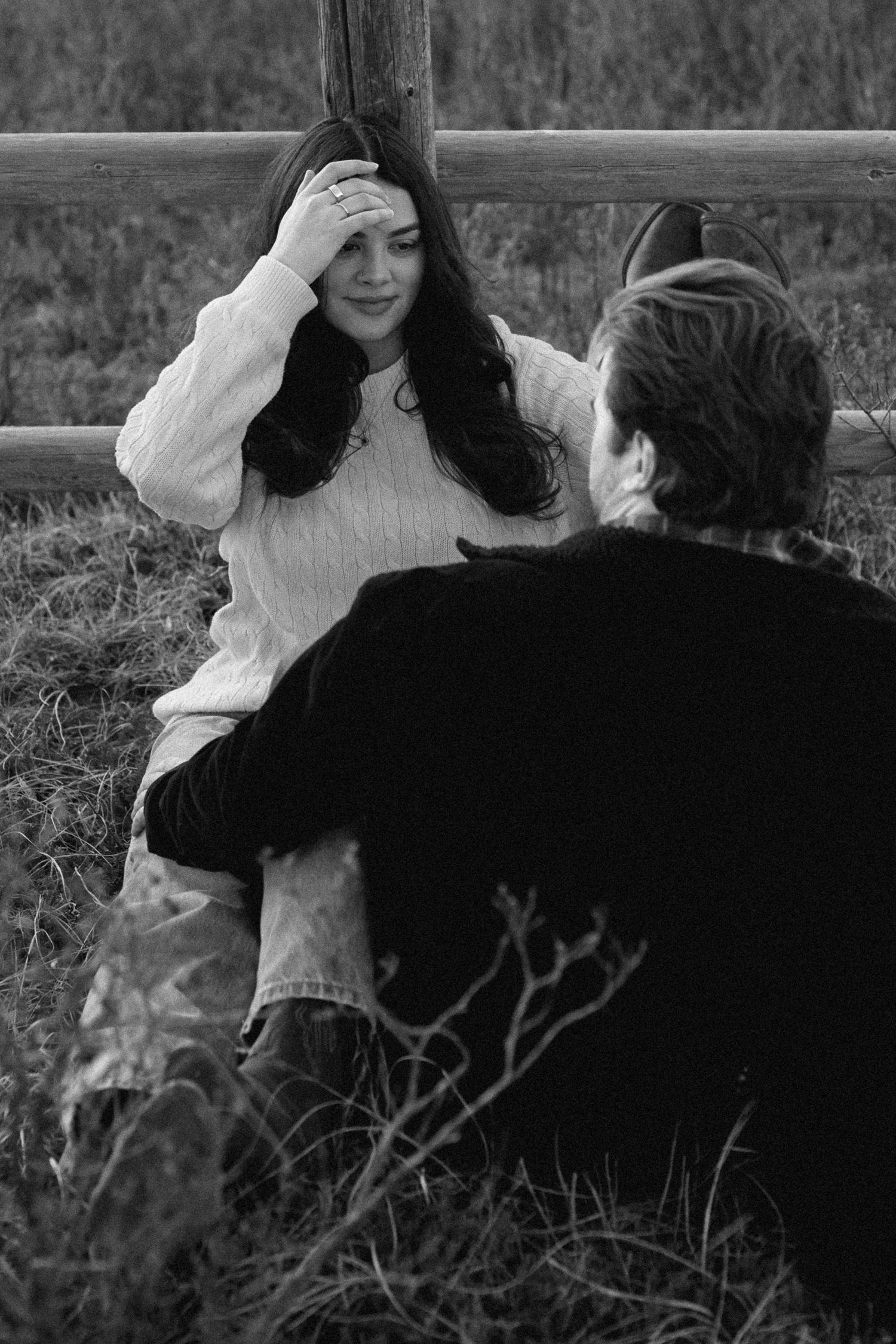 Black and white photo of couple resting by wooden fence in romantic pose.