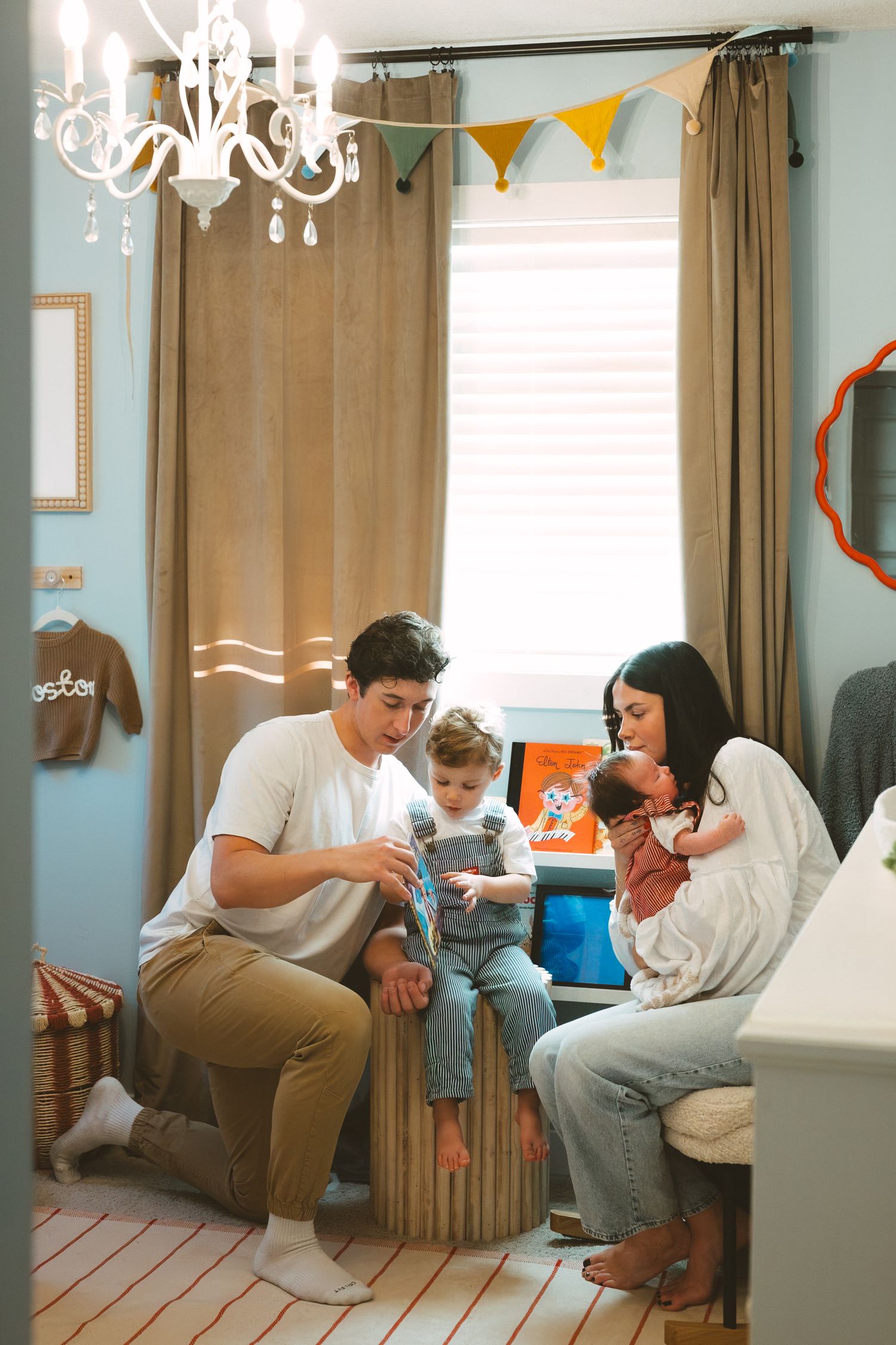 Family members sit together on a couch in a living room decorated with orange bunting and curtains.