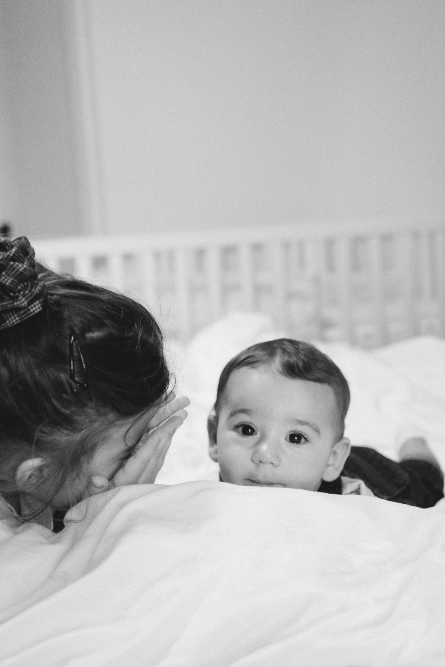 Black and white photo series showing two children lying together on white bedding in various poses.