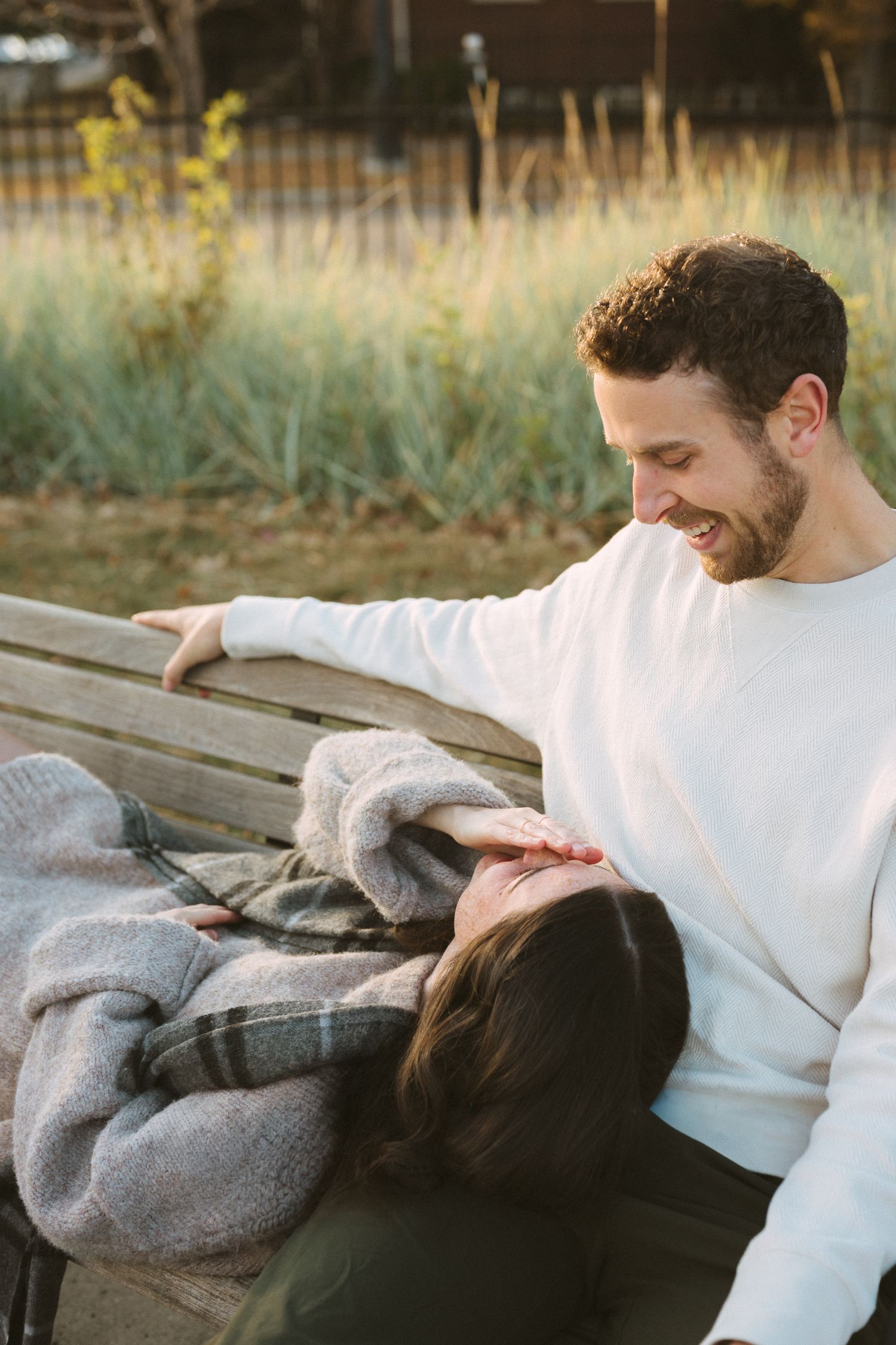 A couple sharing a tender moment together on a wooden bench in an outdoor setting during golden hour.