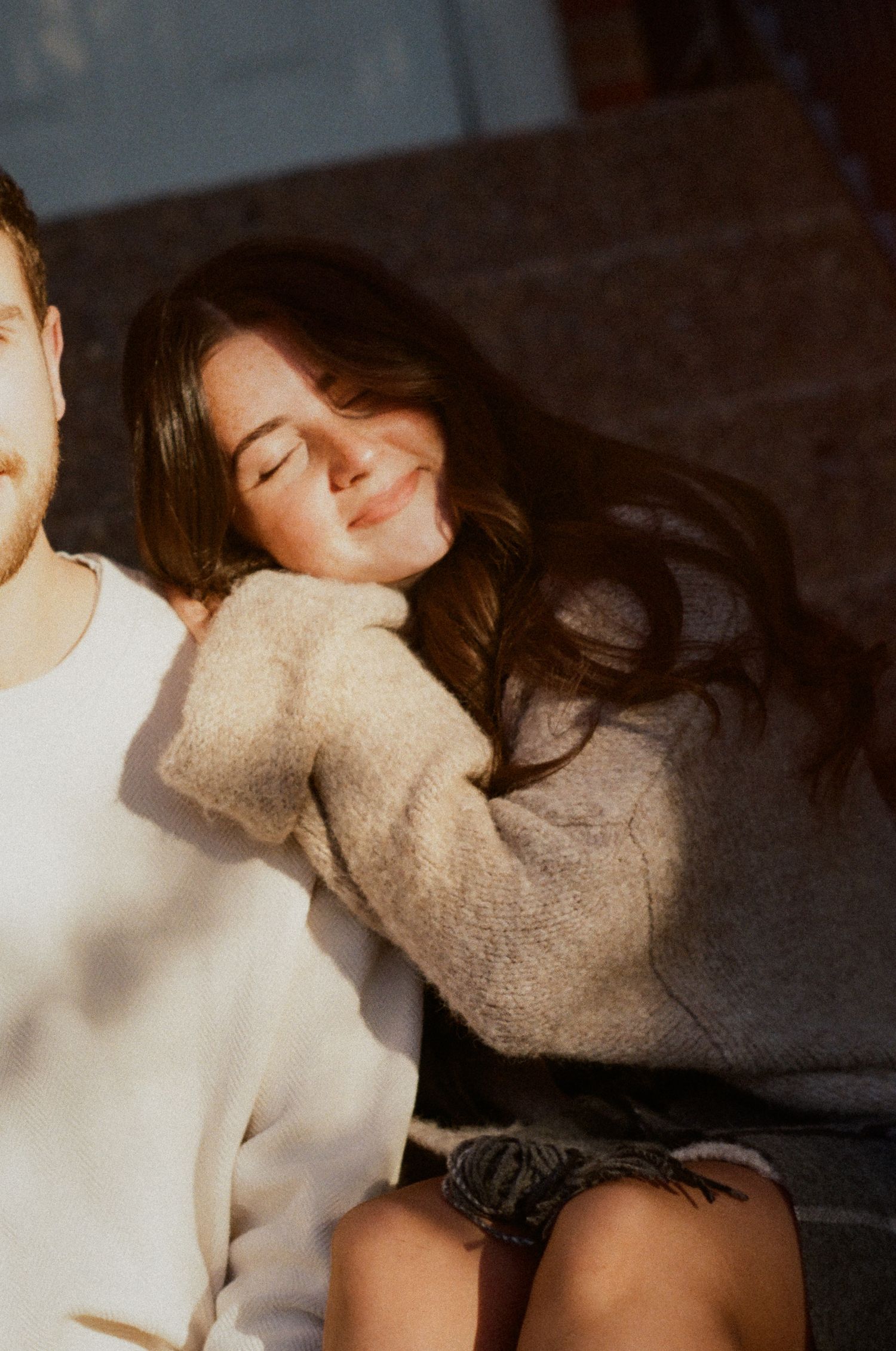 A person in a beige sweater lies down with closed eyes in a dimly lit setting.