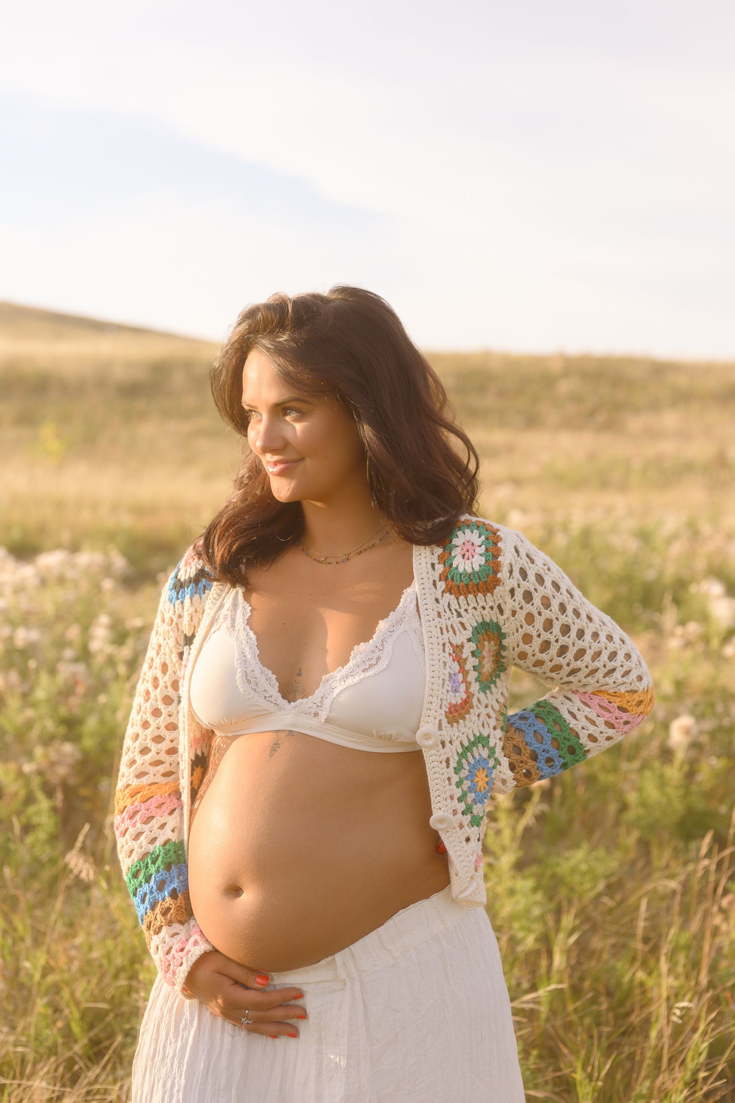 A joyful maternity portrait featuring a colorful crochet sweater in a sun-lit wildflower field.