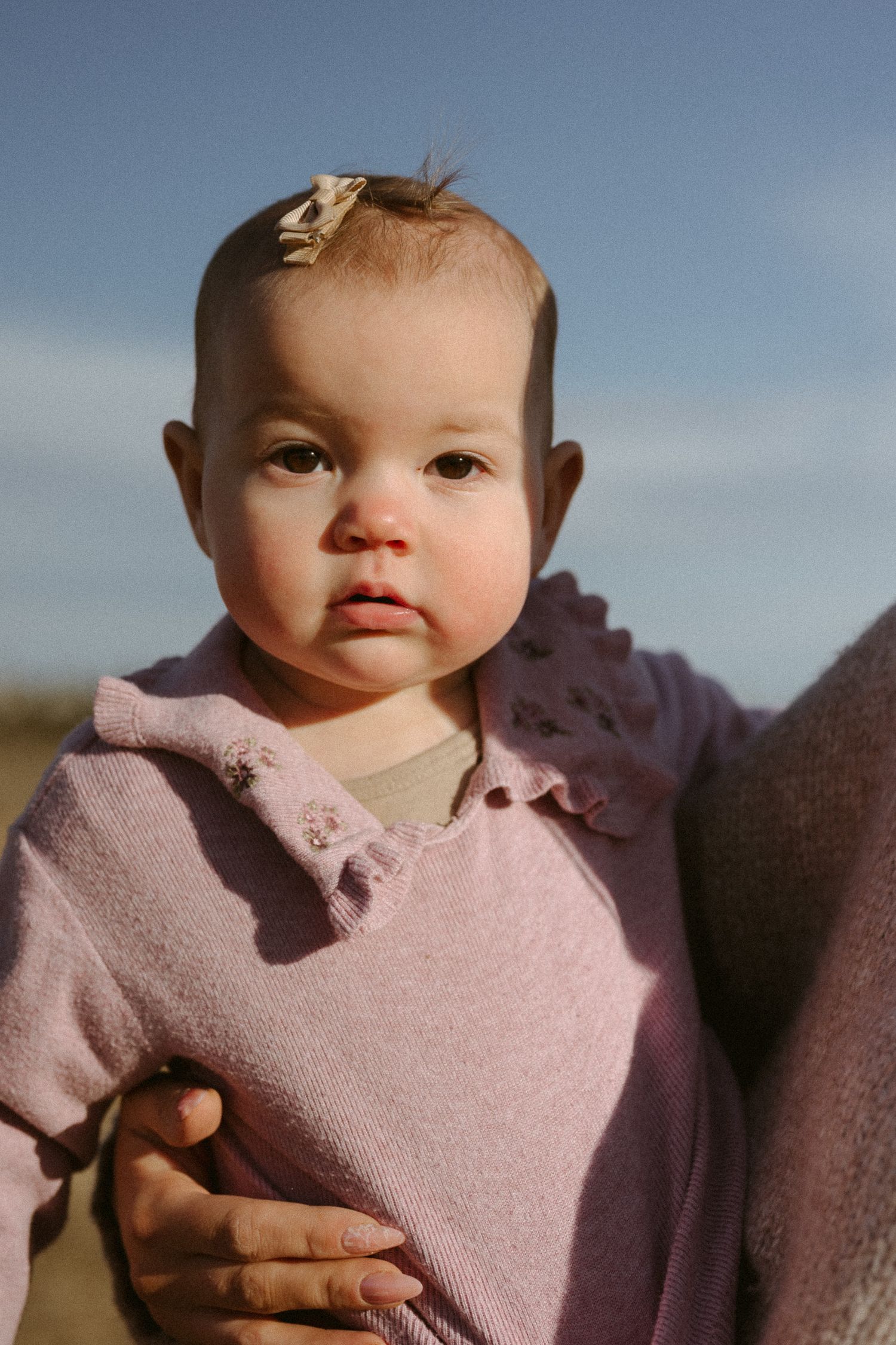 Close-up portrait of a baby wearing a soft pink fleece jacket outdoors.