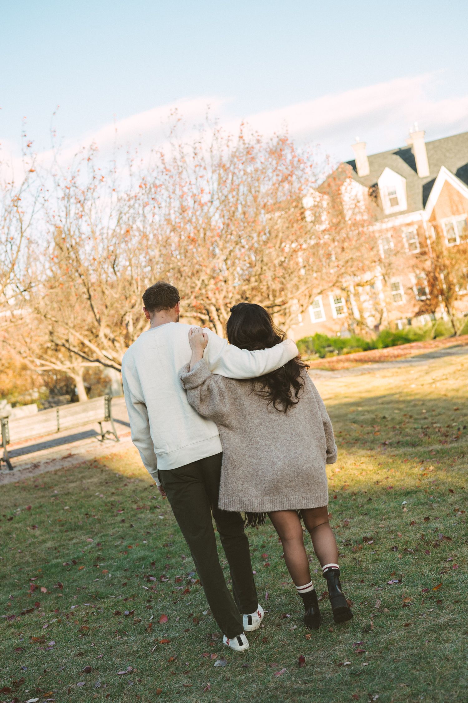 A couple walks together on a grassy hillside during golden hour, sharing a tender moment in autumn.