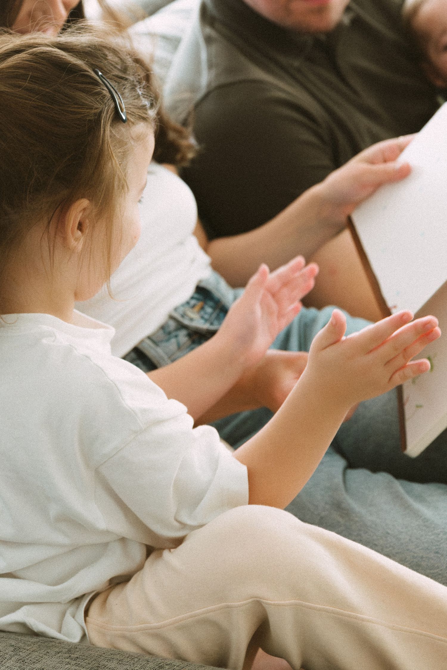 Child in white shirt reaching towards books while sitting on a couch during storytime.