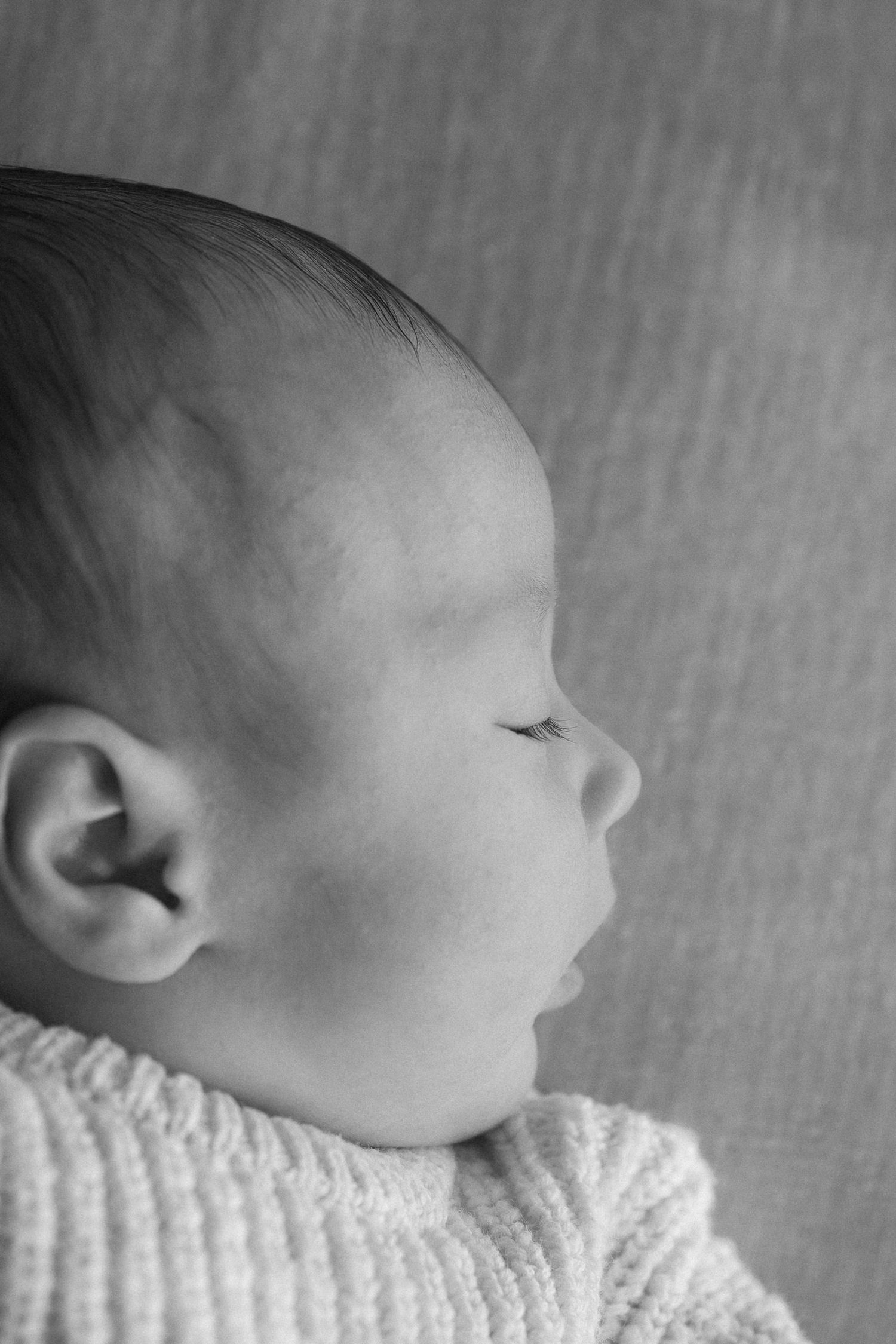 Close-up profile view of an infant wearing a white knit sweater in black and white.