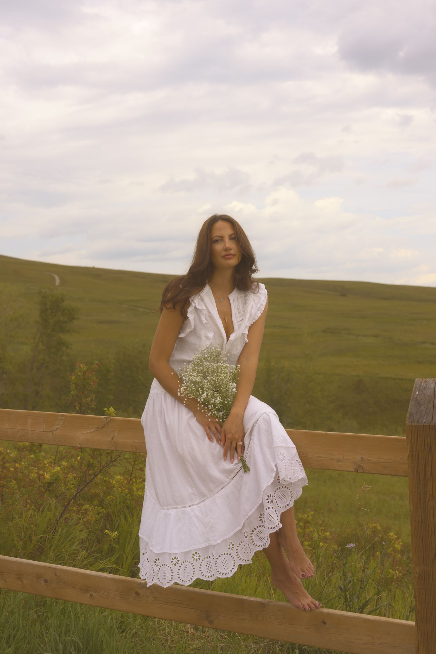 Rustic outdoor scene with white eyelet dress against a pastoral landscape.