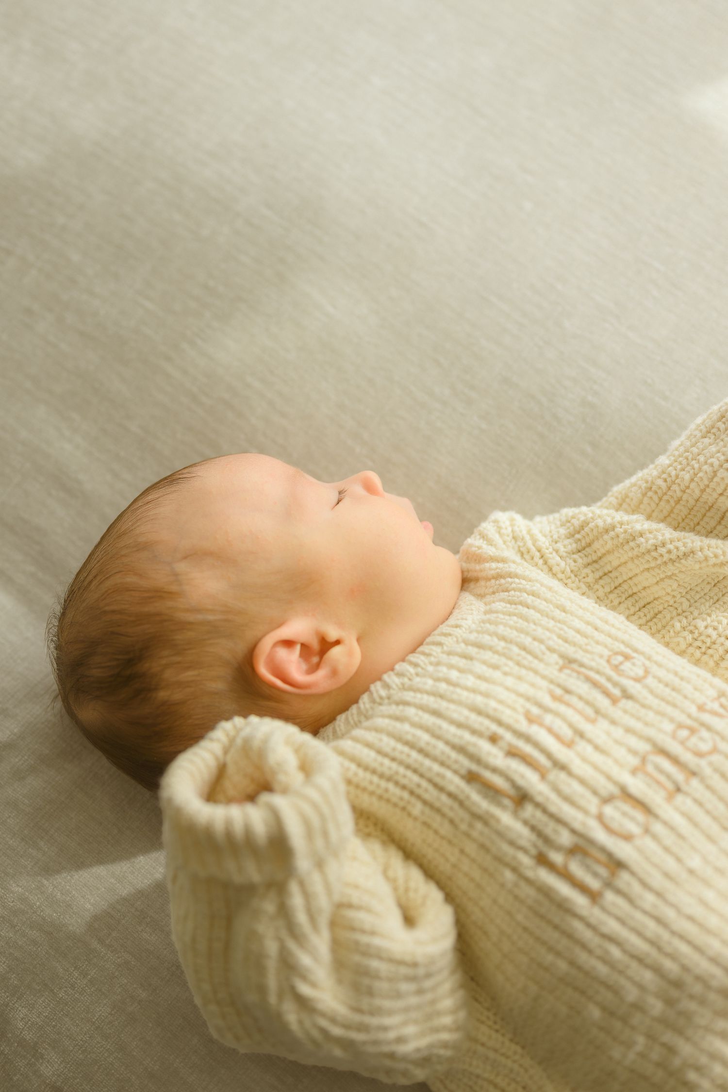 Sleeping newborn wrapped in cream colored knit blanket.