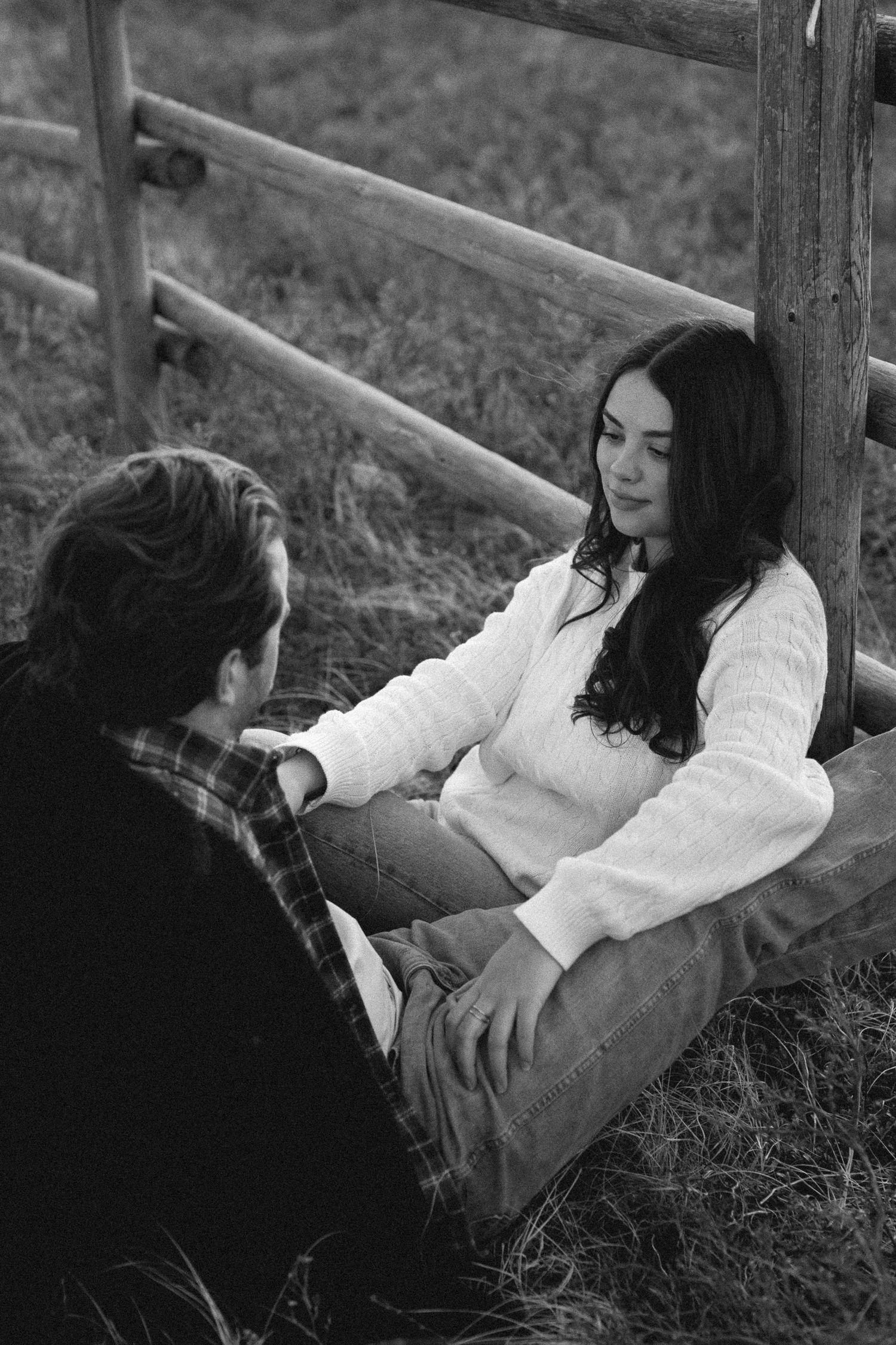 Couple lying together on grass by wooden fence sharing an intimate moment in black and white.
