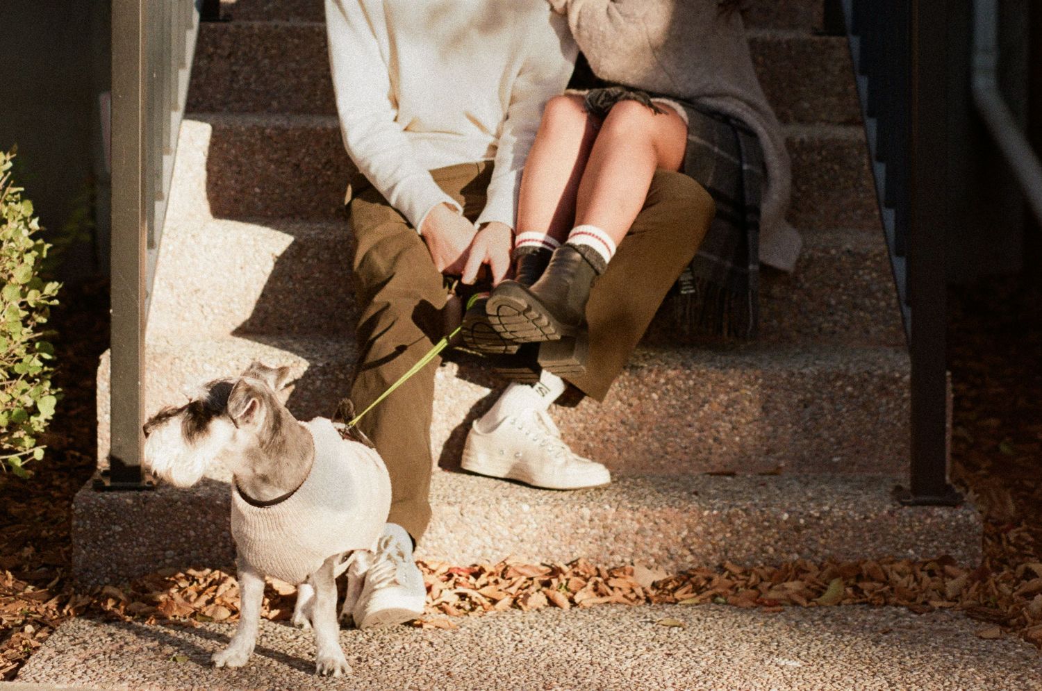 Close-up view of feet and shoes sitting on concrete steps with fallen leaves scattered around.