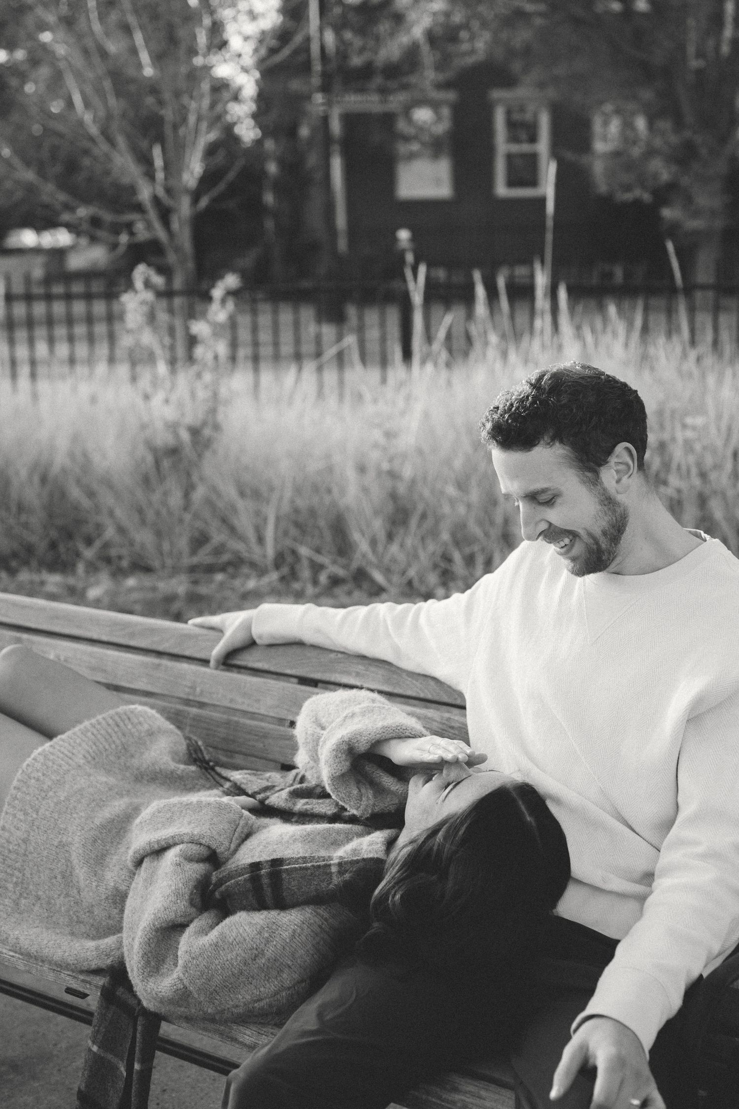 A couple lounges peacefully on a park bench with fall foliage in the background.