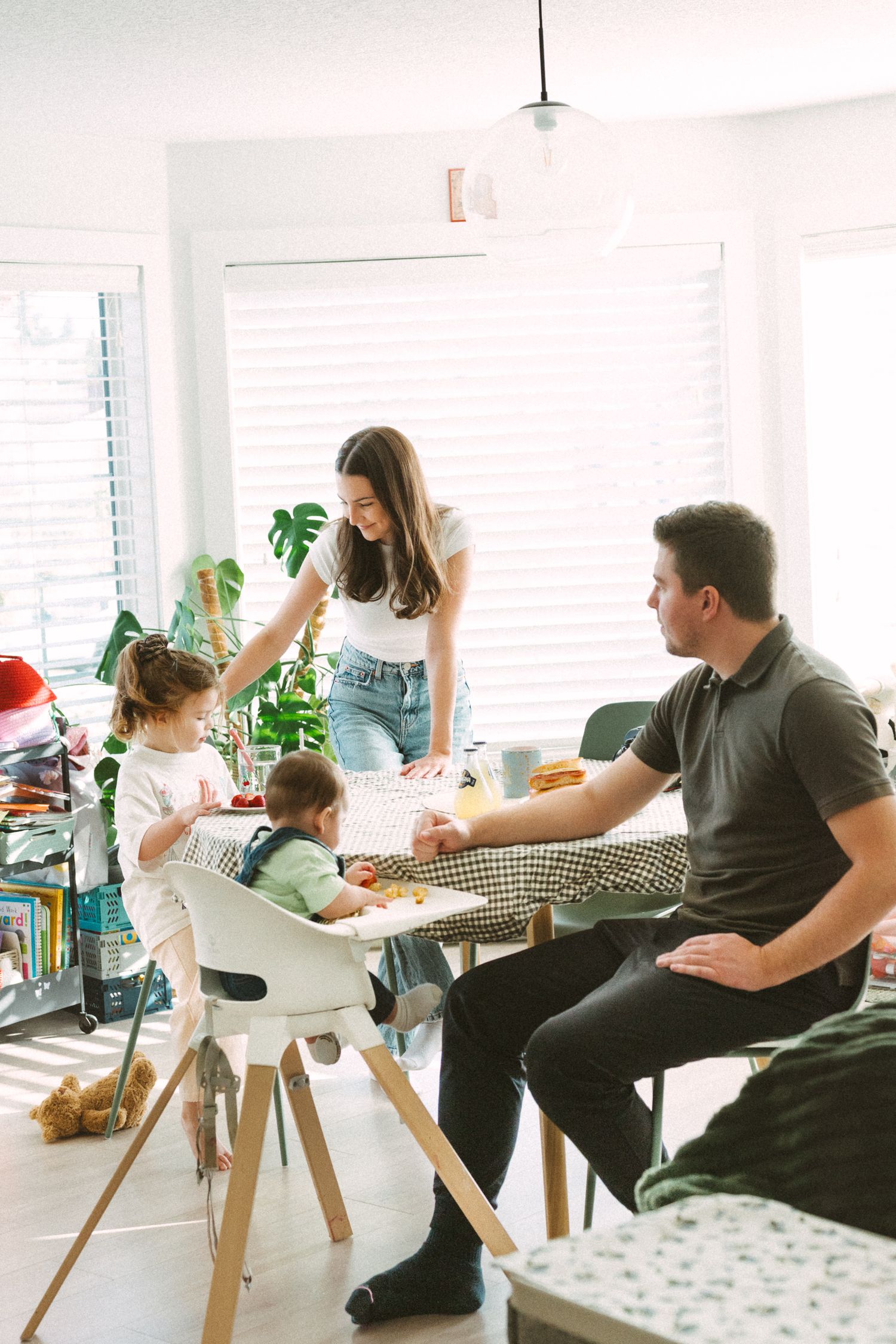 People gather around a wooden table in a bright modern living room with white walls and houseplants.