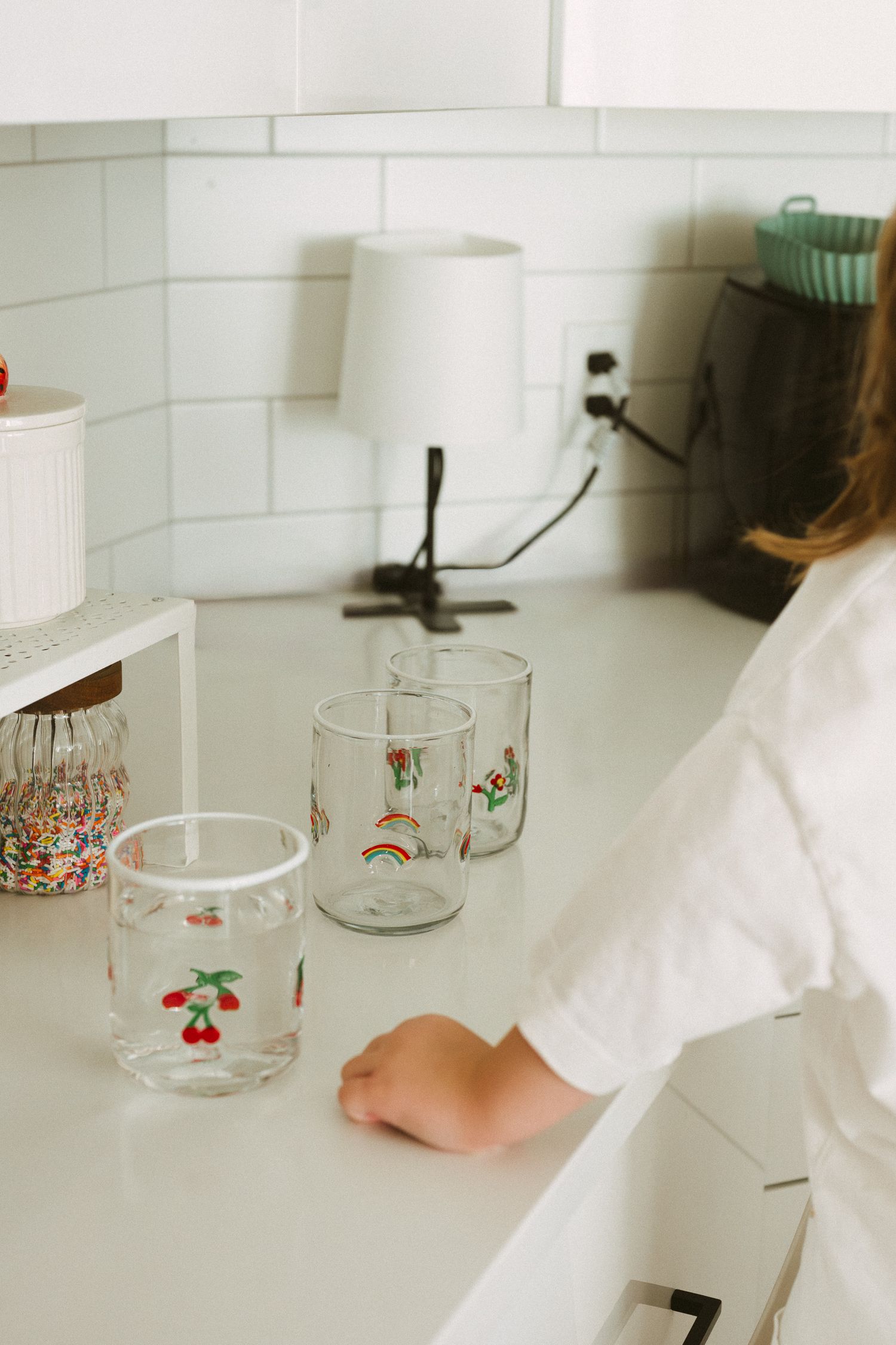 A sequence of glass cups with vintage floral patterns being arranged on a white counter surface.