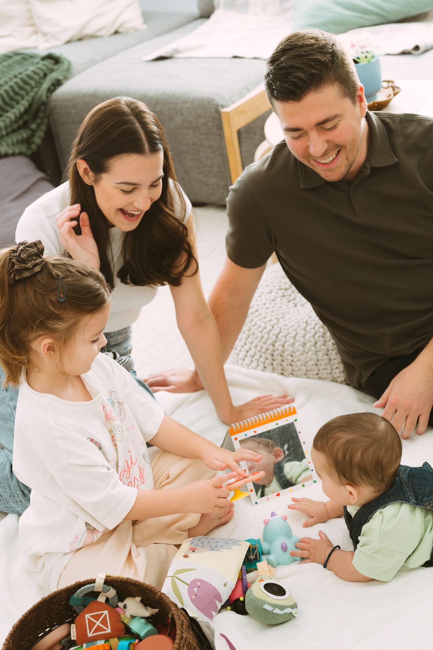 Parents and child playing together with toys on a white bed during a casual family moment.