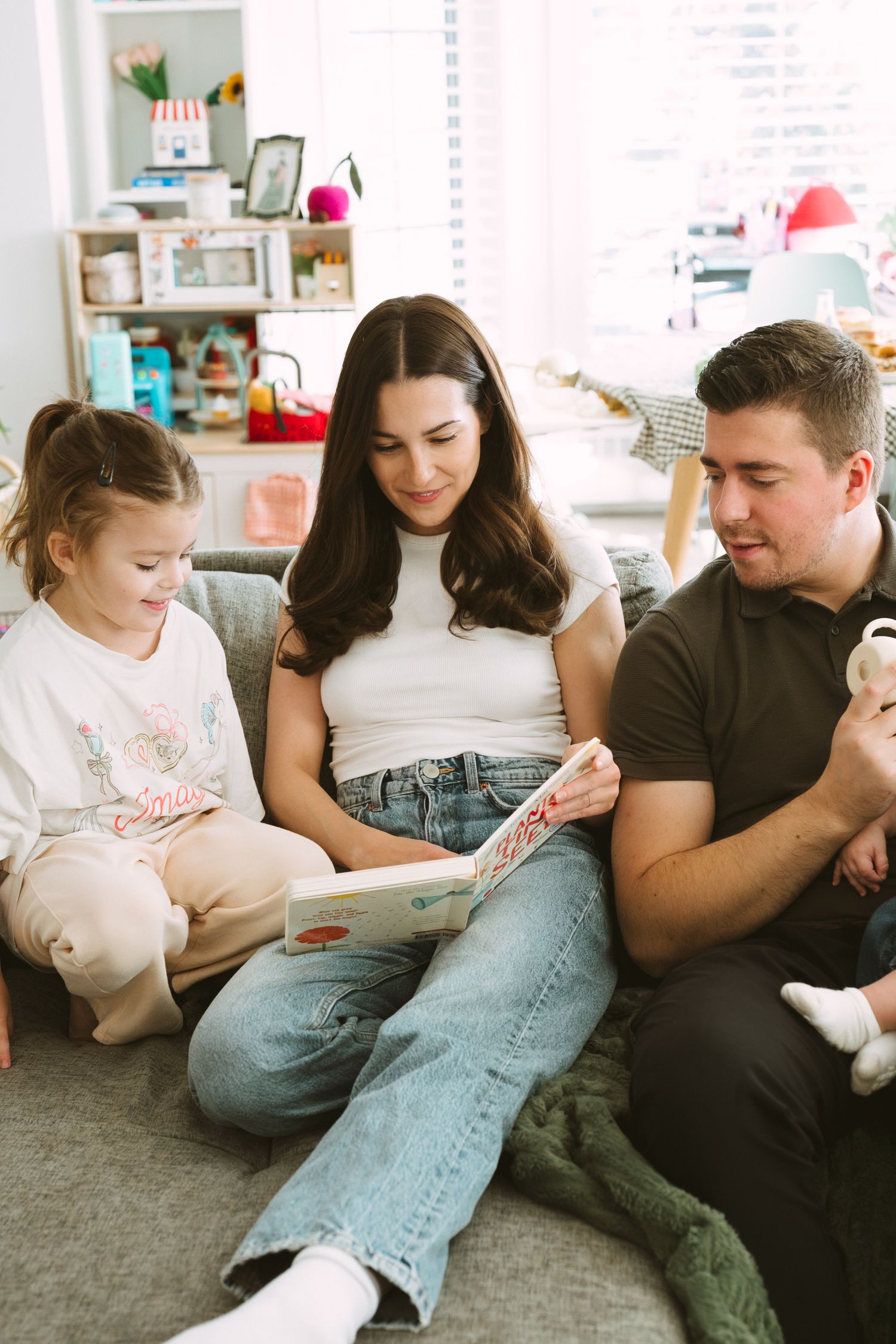 A family lounges together on a gray couch in a bright, modern living room.