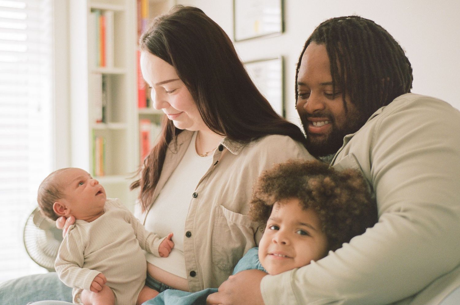 Happy interracial family of four with newborn and curly-haired toddler sharing a joyful moment.