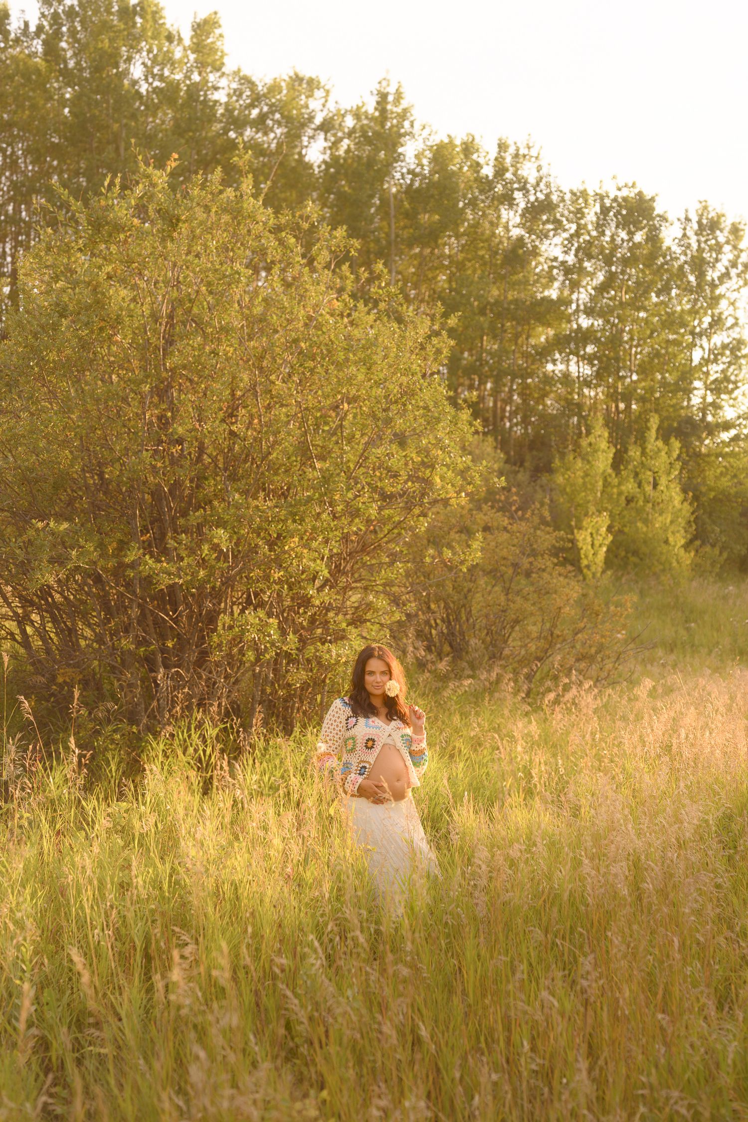 A dreamy sunset photoshoot in a golden field with tall grass and trees in the background.