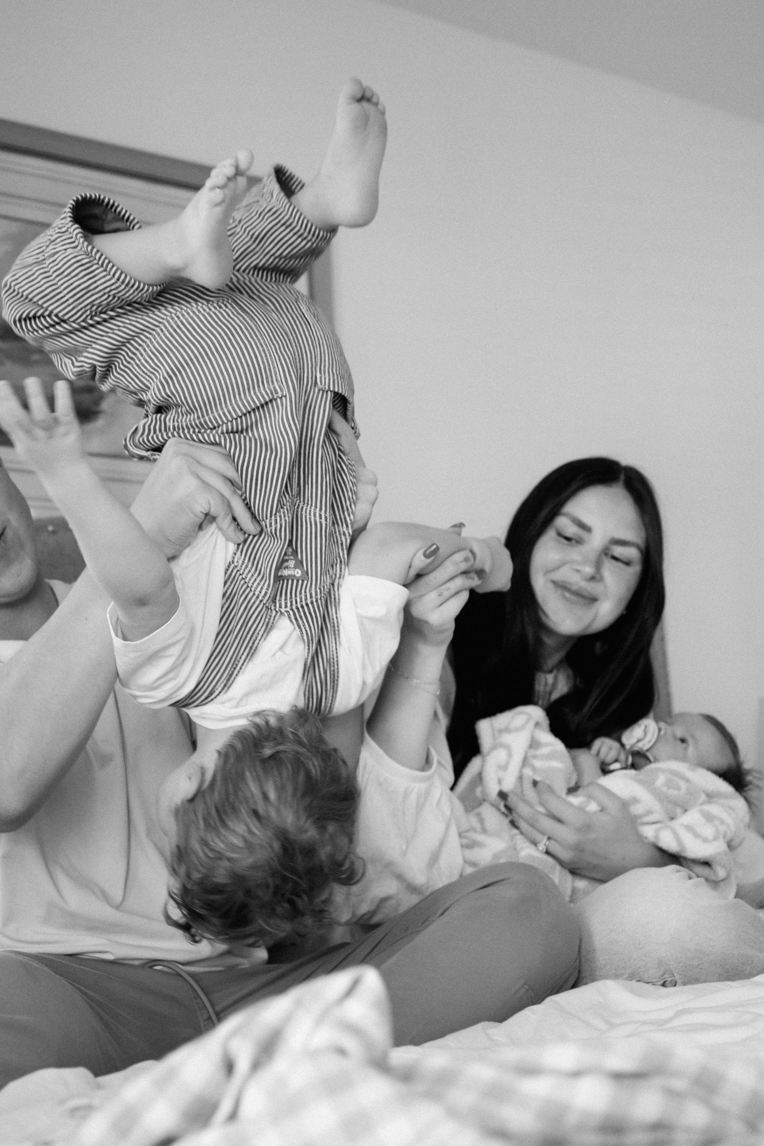 Black and white photos showing playful moments between a baby and caregiver on a bed.
