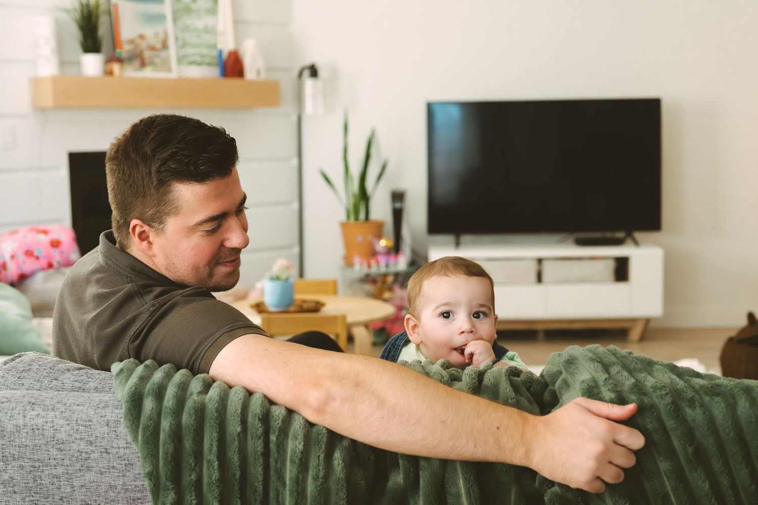 Family relaxing together on a green velvet couch in a bright modern living room.