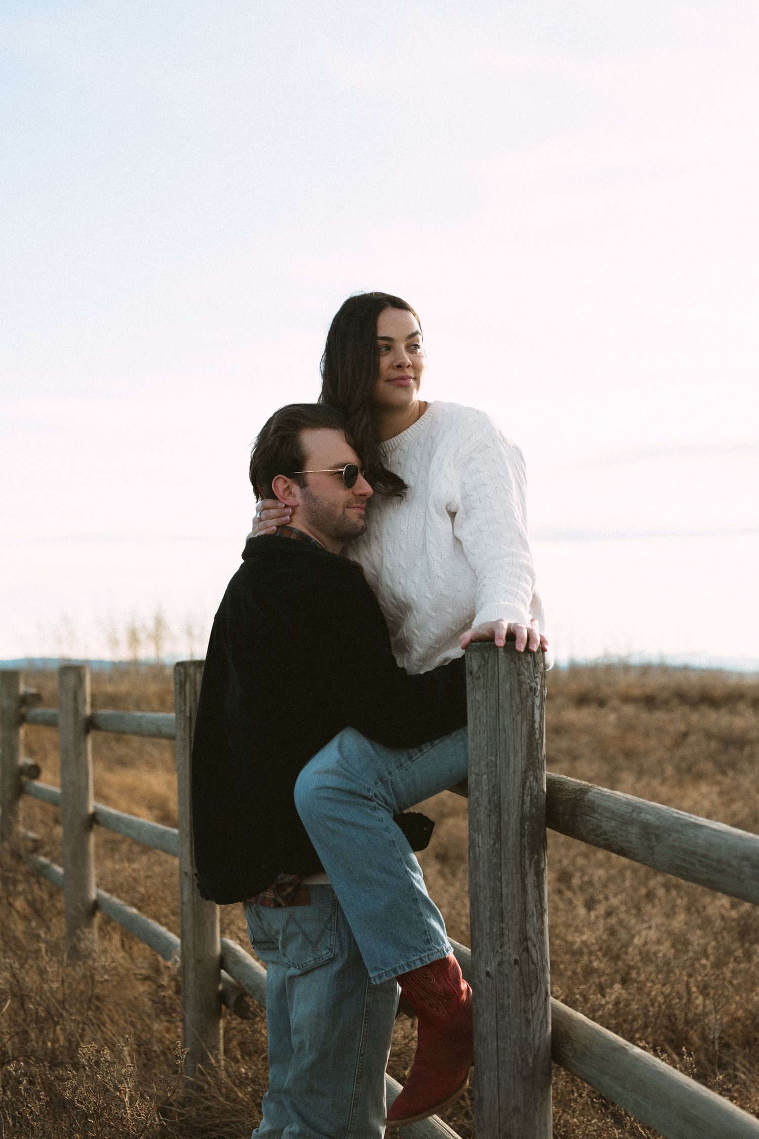 Two people sharing an intimate moment while sitting on a rustic fence in the countryside.