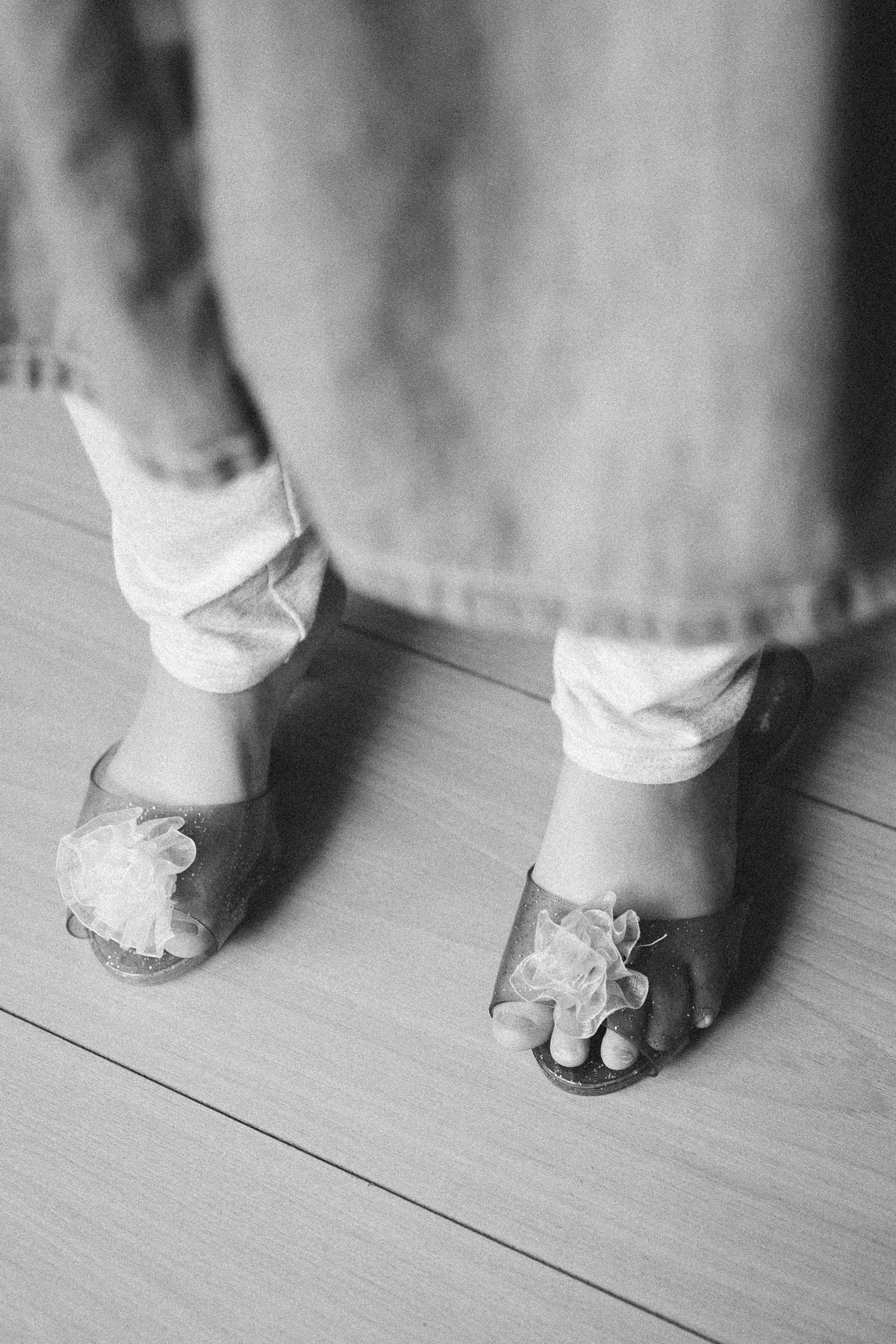 Black and white photo of a young child wearing decorative sandals with floral details and white leggings.