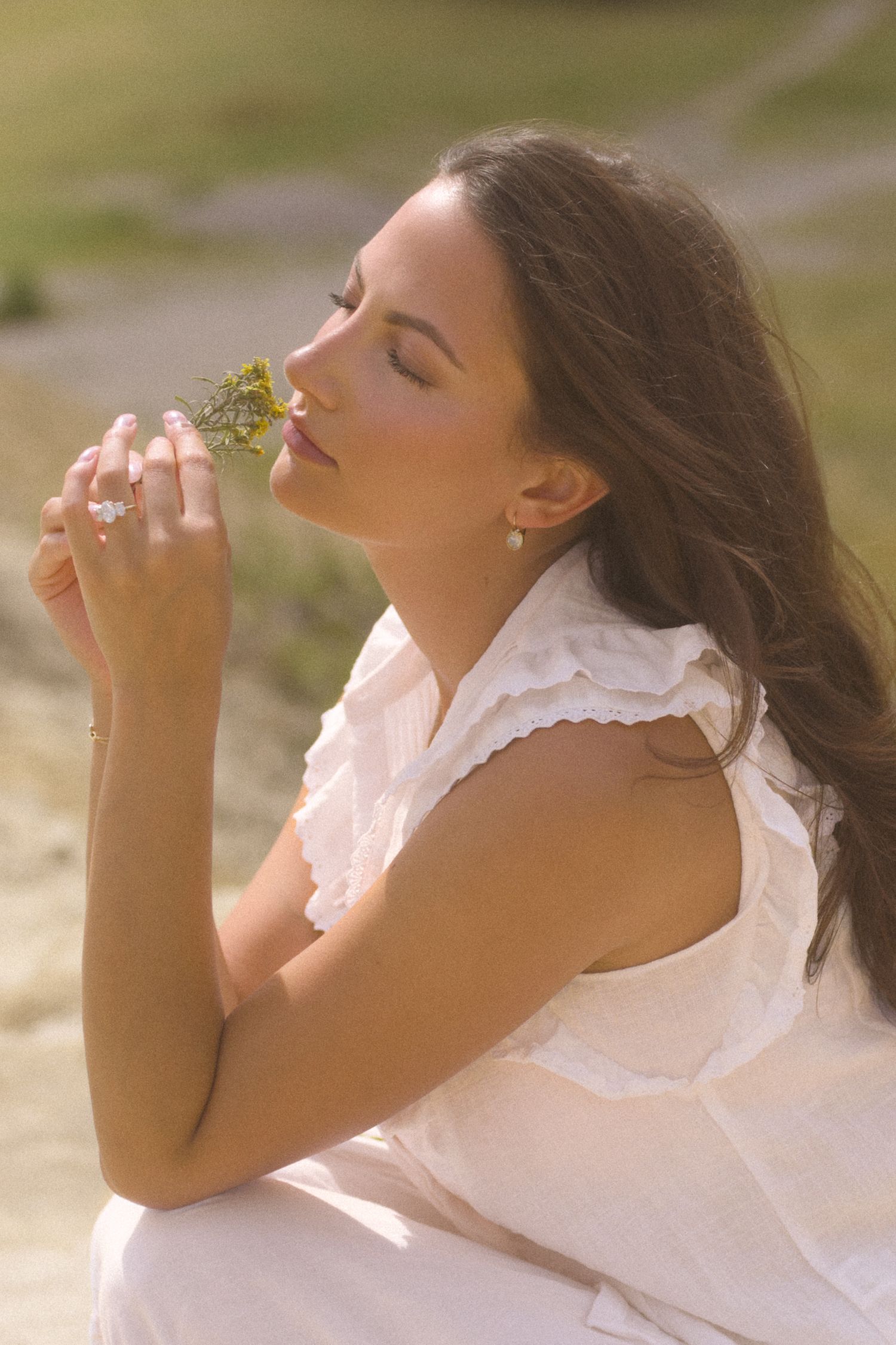 A person in white lace holds flowers to their face while basking in golden sunlight.