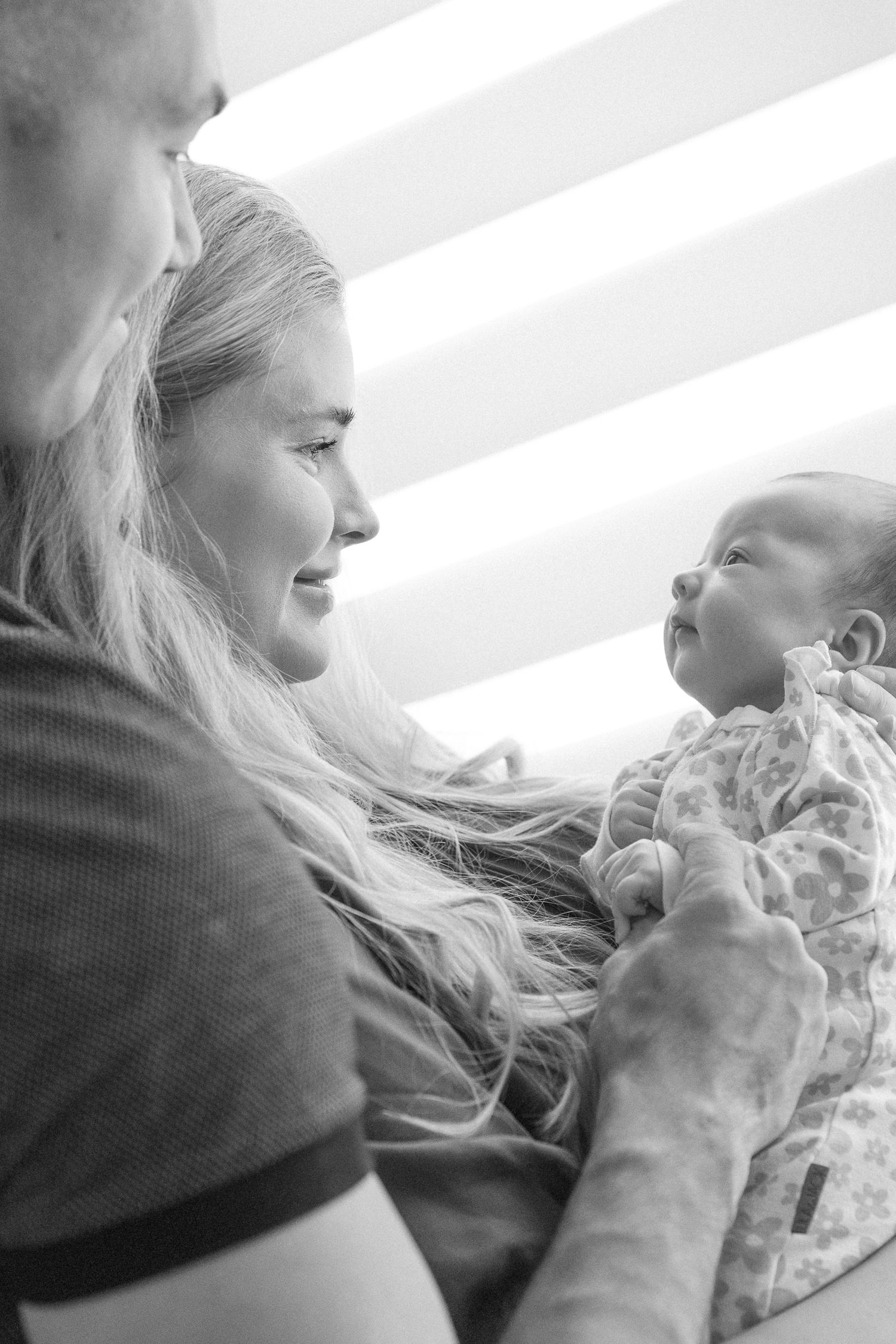 Side profile of loving parents cradling their newborn in natural window light.