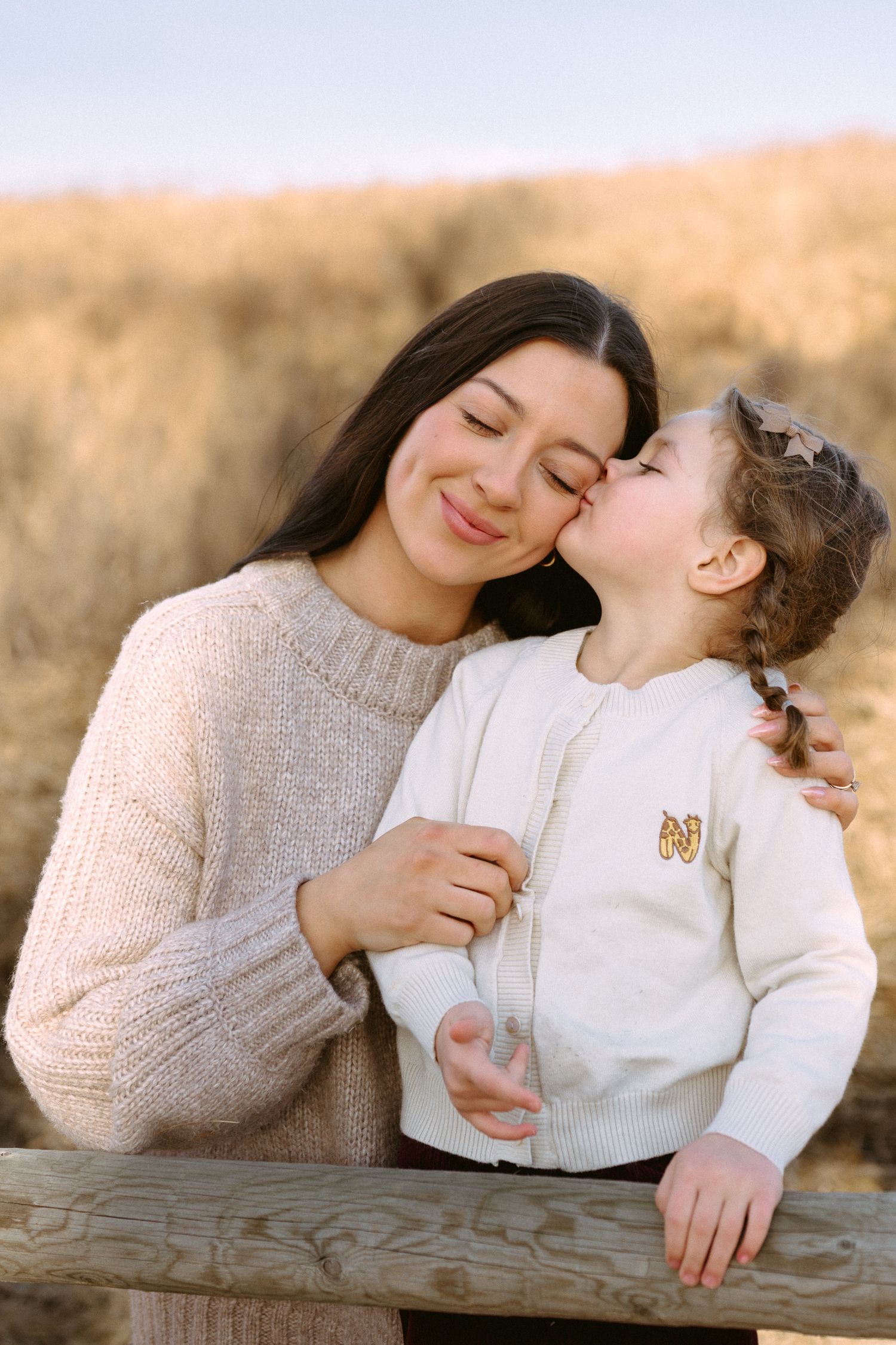 A tender moment between parent and child as they share affection while leaning on a wooden fence.