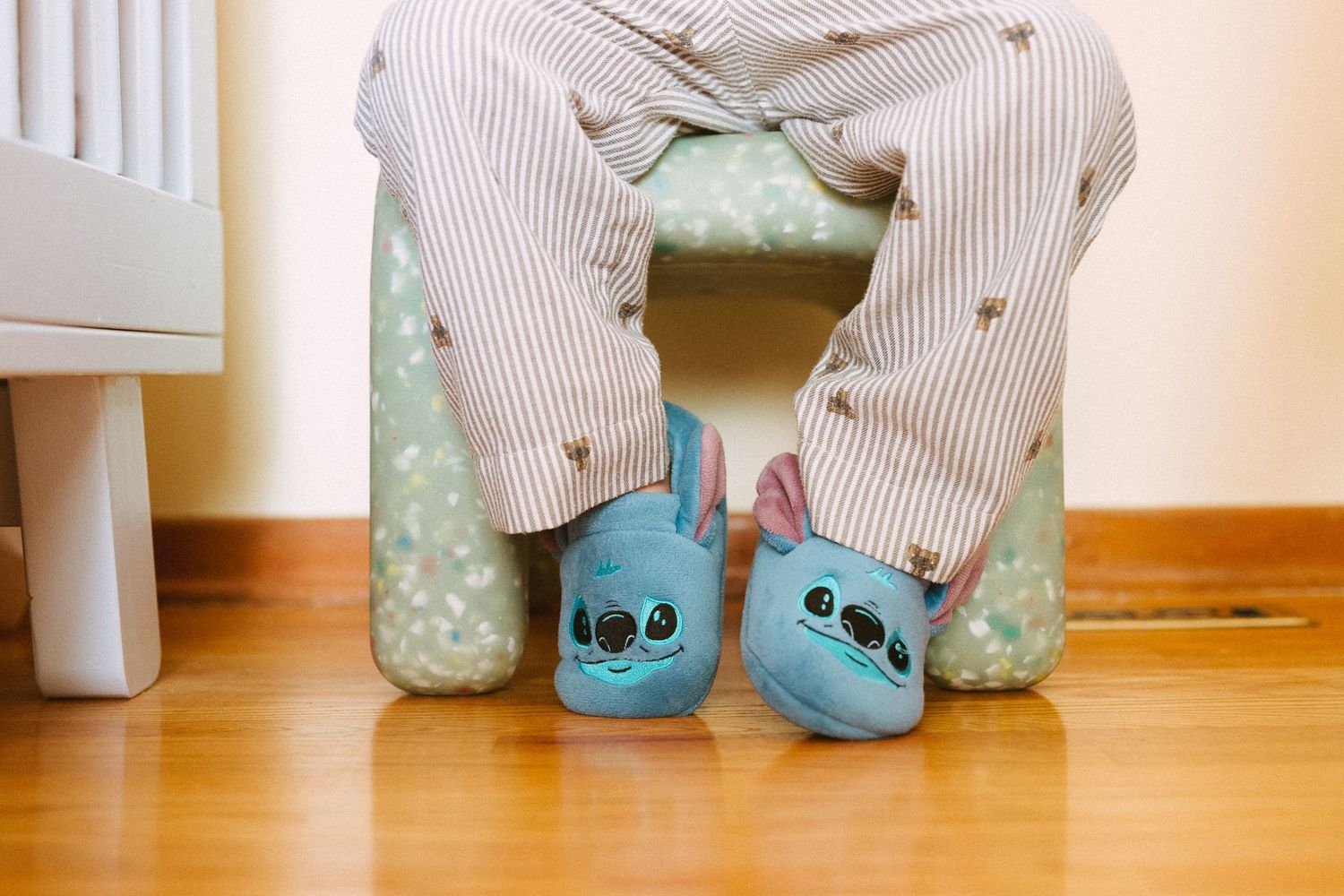 Blue Stitch character slippers shown with striped pants on wooden floor.